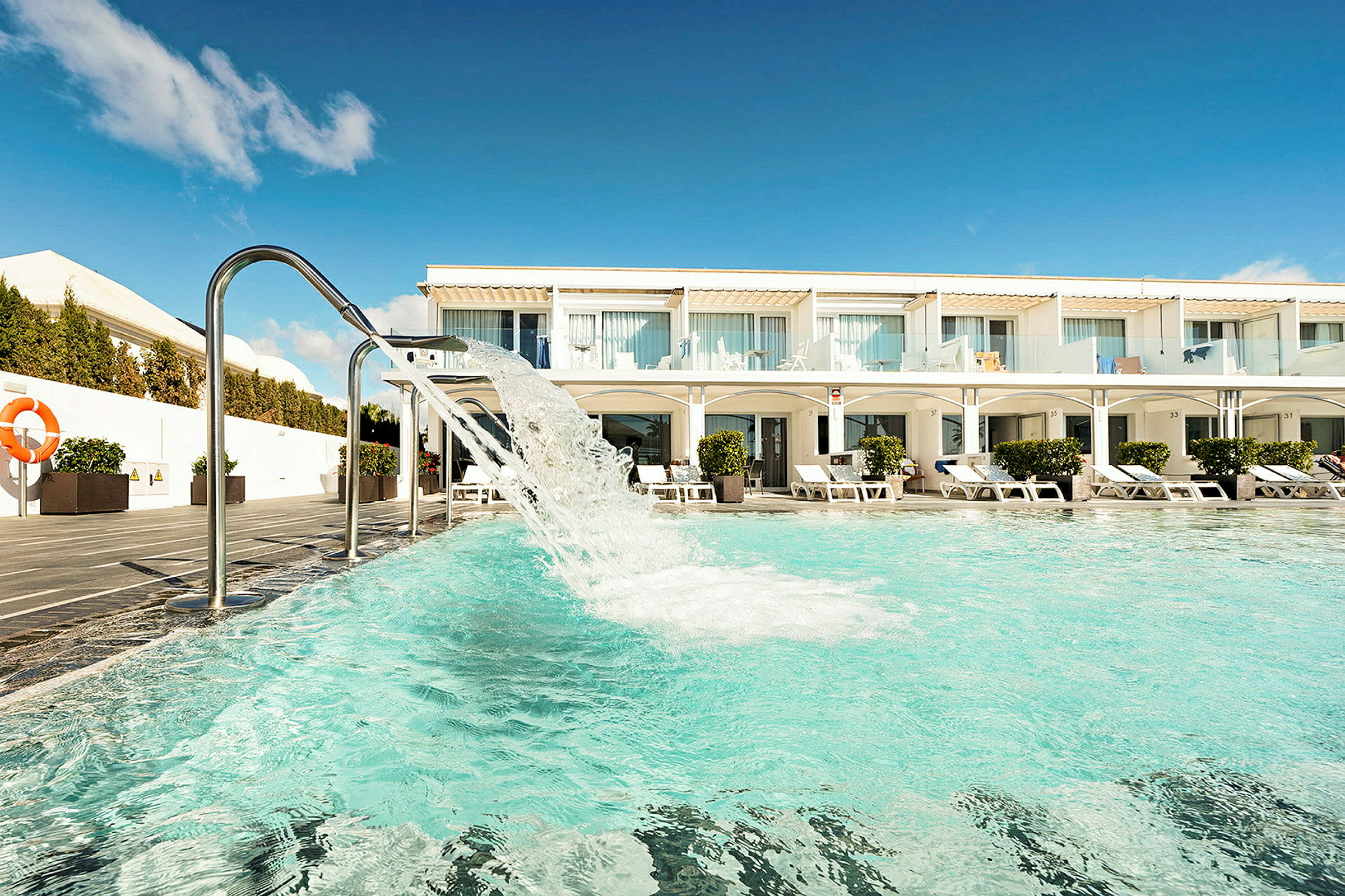 Poolområde med liggestole og en hotelbygning i baggrunden. (AI-genereret tekst)