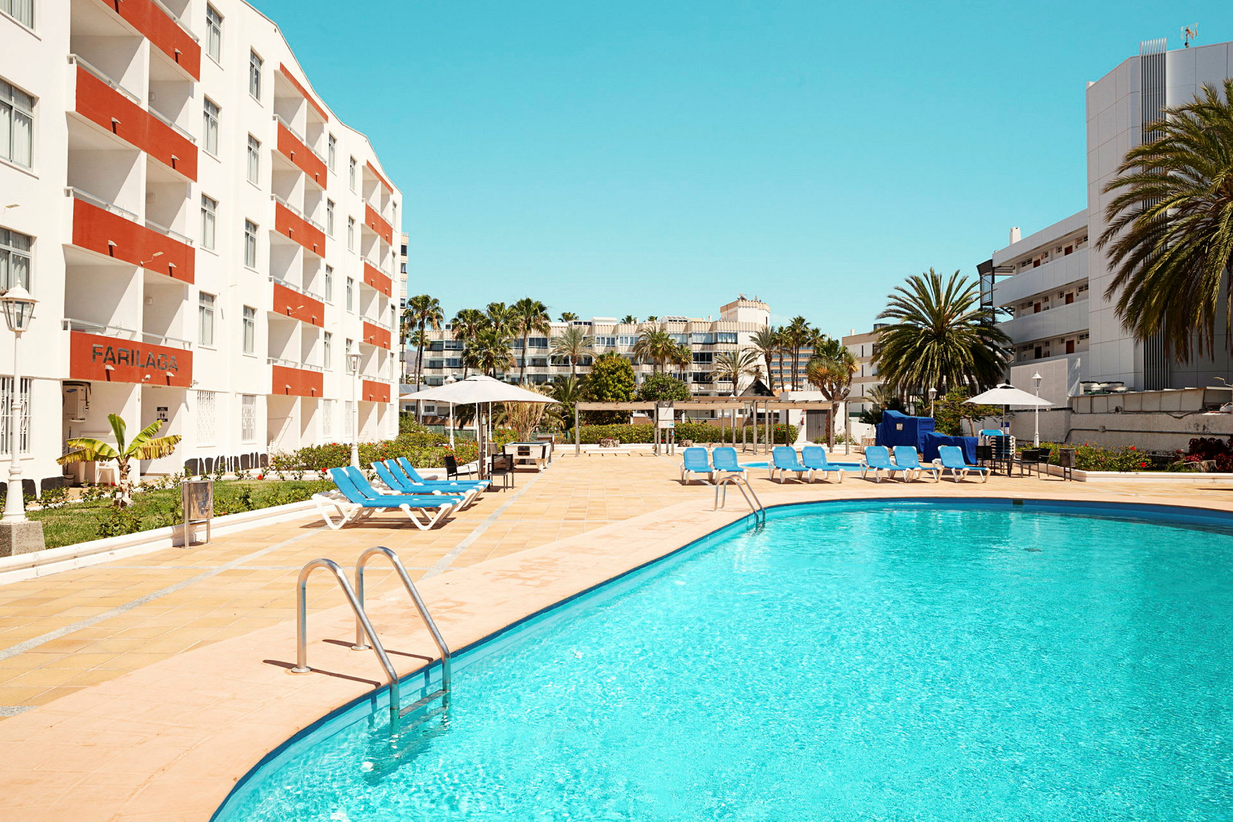 Udendørs pool med solsenge og omkringliggende hotelbygninger. (AI-genereret tekst)