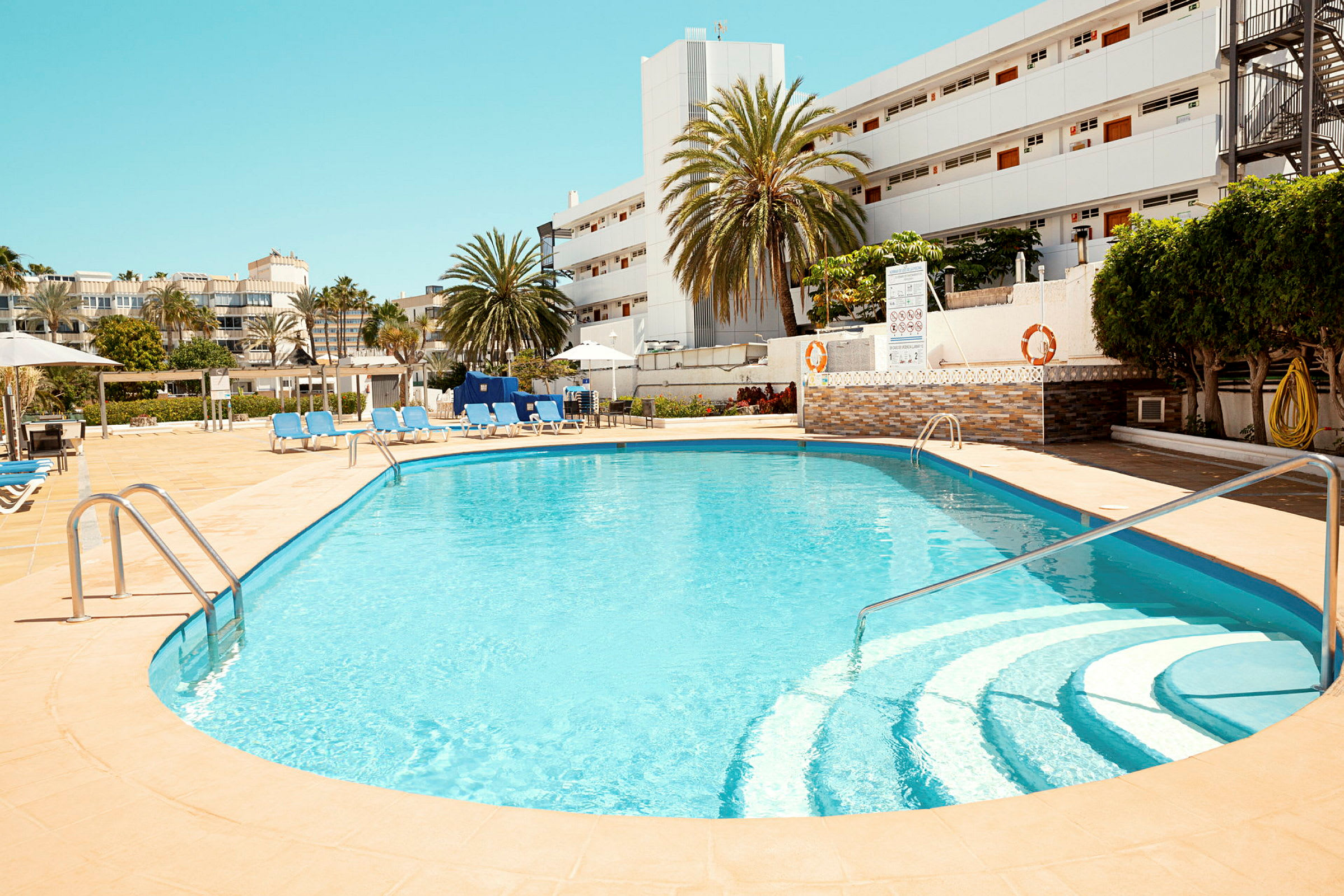 Udendørs swimmingpool med stole og liggestole omkring, i hotelmiljø. (AI-genereret tekst)