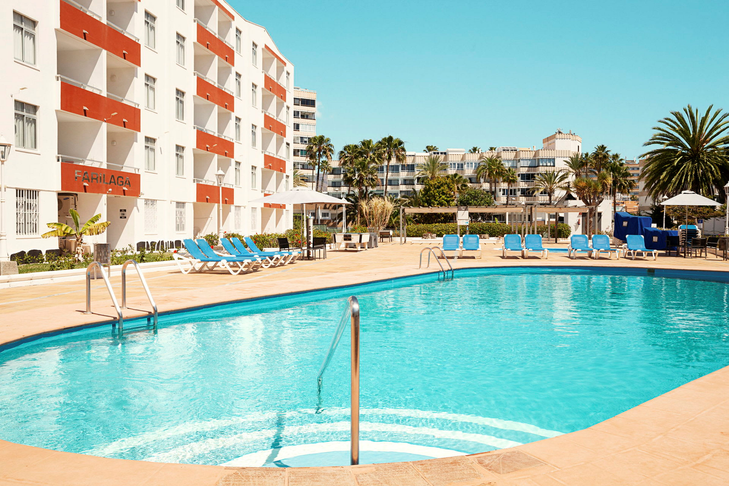 En udendørs pool med liggestole ved et hotel. (AI-genereret tekst)