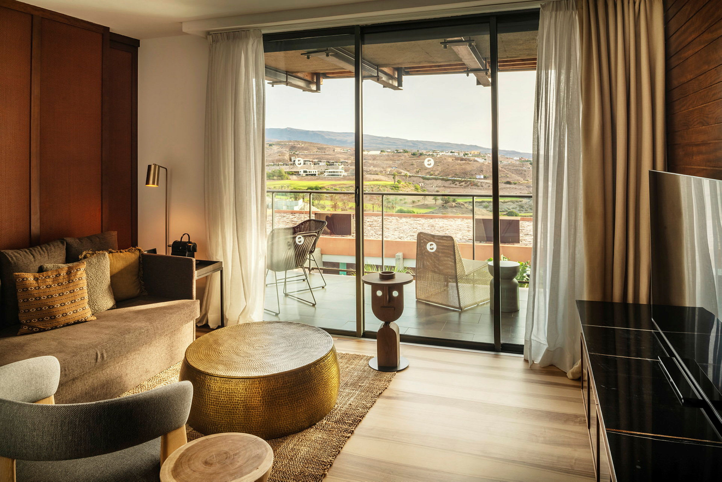 En indrettet hotelsuite med en siddegruppe og udsigt til en balkon og landskab. (AI-genereret tekst)
