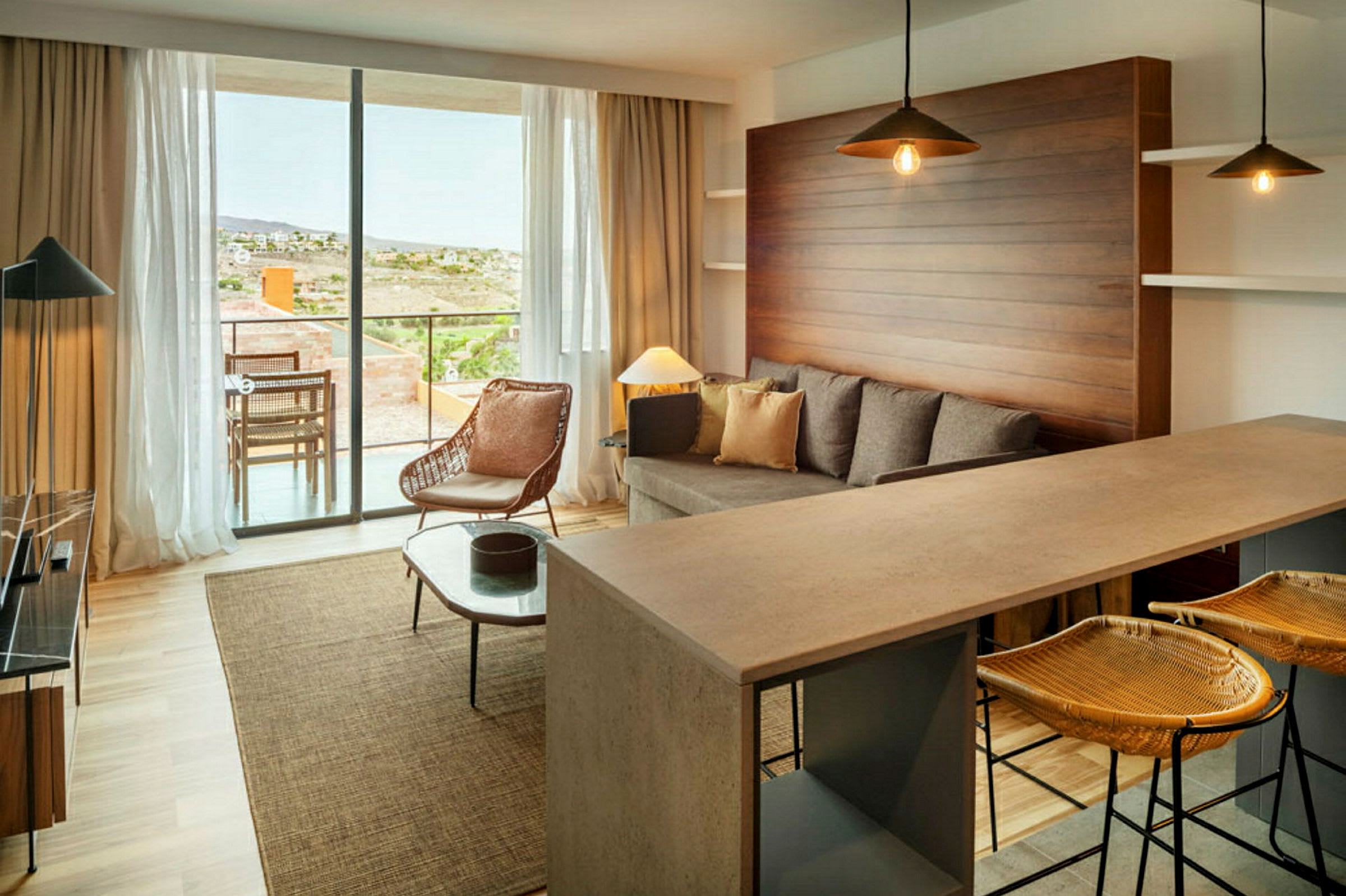 En moderne stue med sofa, lænestol og køkkenbar. Store vinduer vender ud mod en terrasse. (AI-genereret tekst)