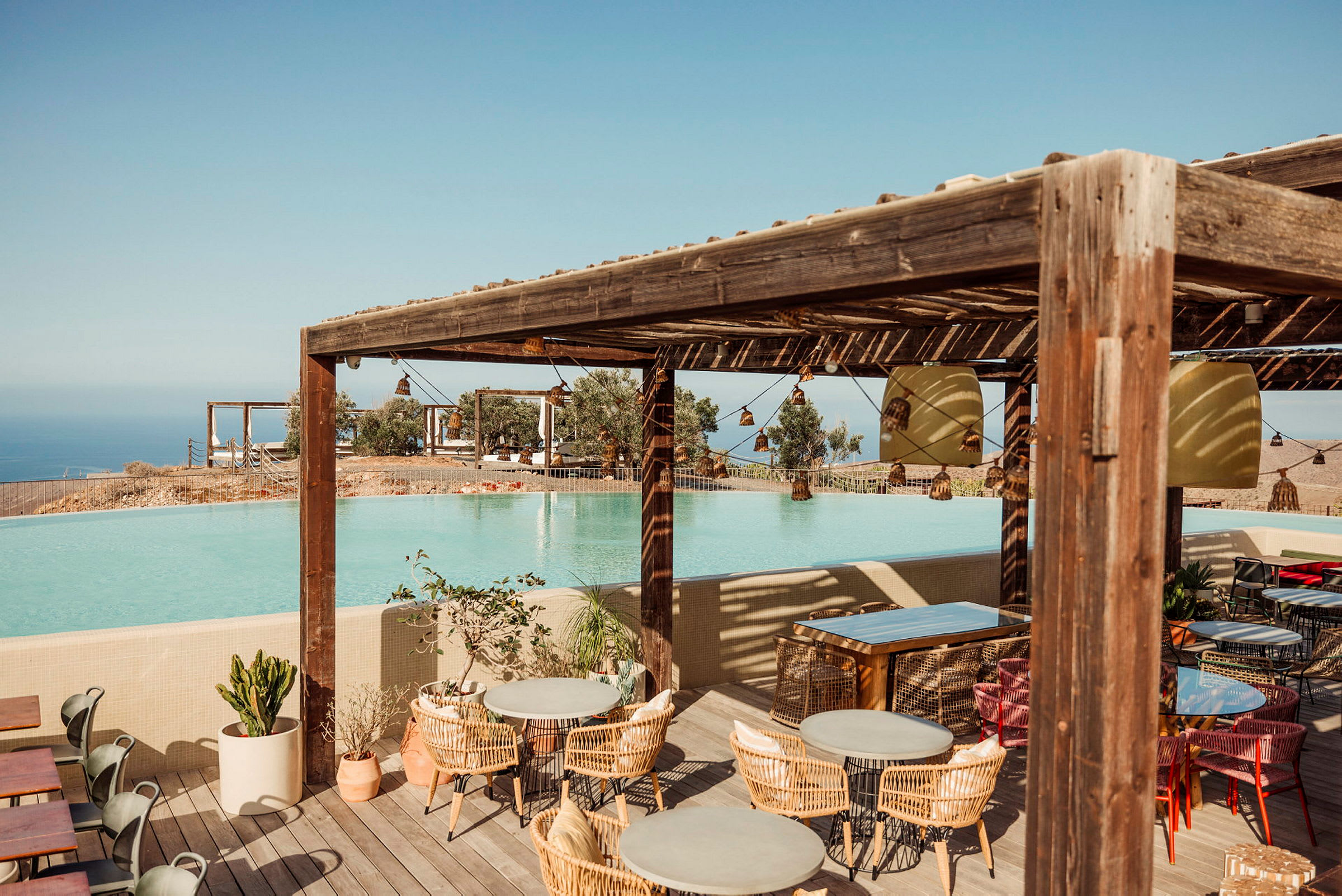 En udendørsrestaurant med udsigt over en pool og havet i baggrunden. (AI-genereret tekst)