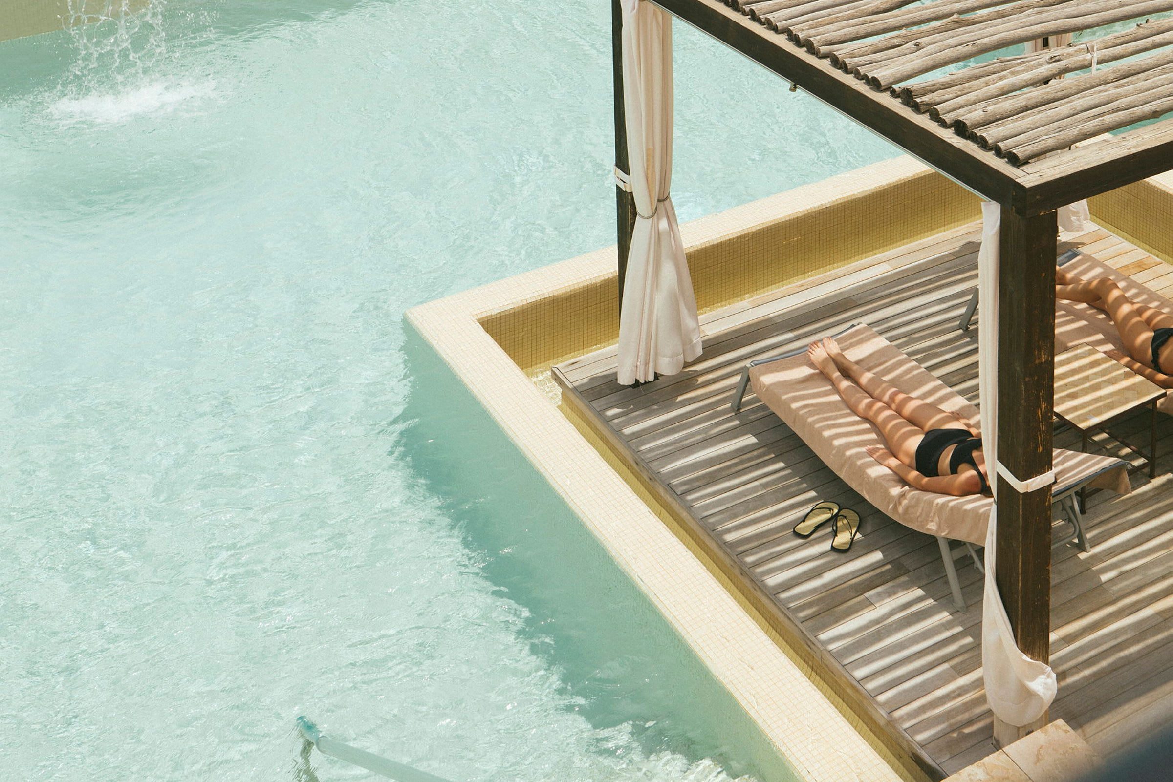 En person ligger på en solvogn i skyggen ved en swimmingpool. (AI-genereret tekst)