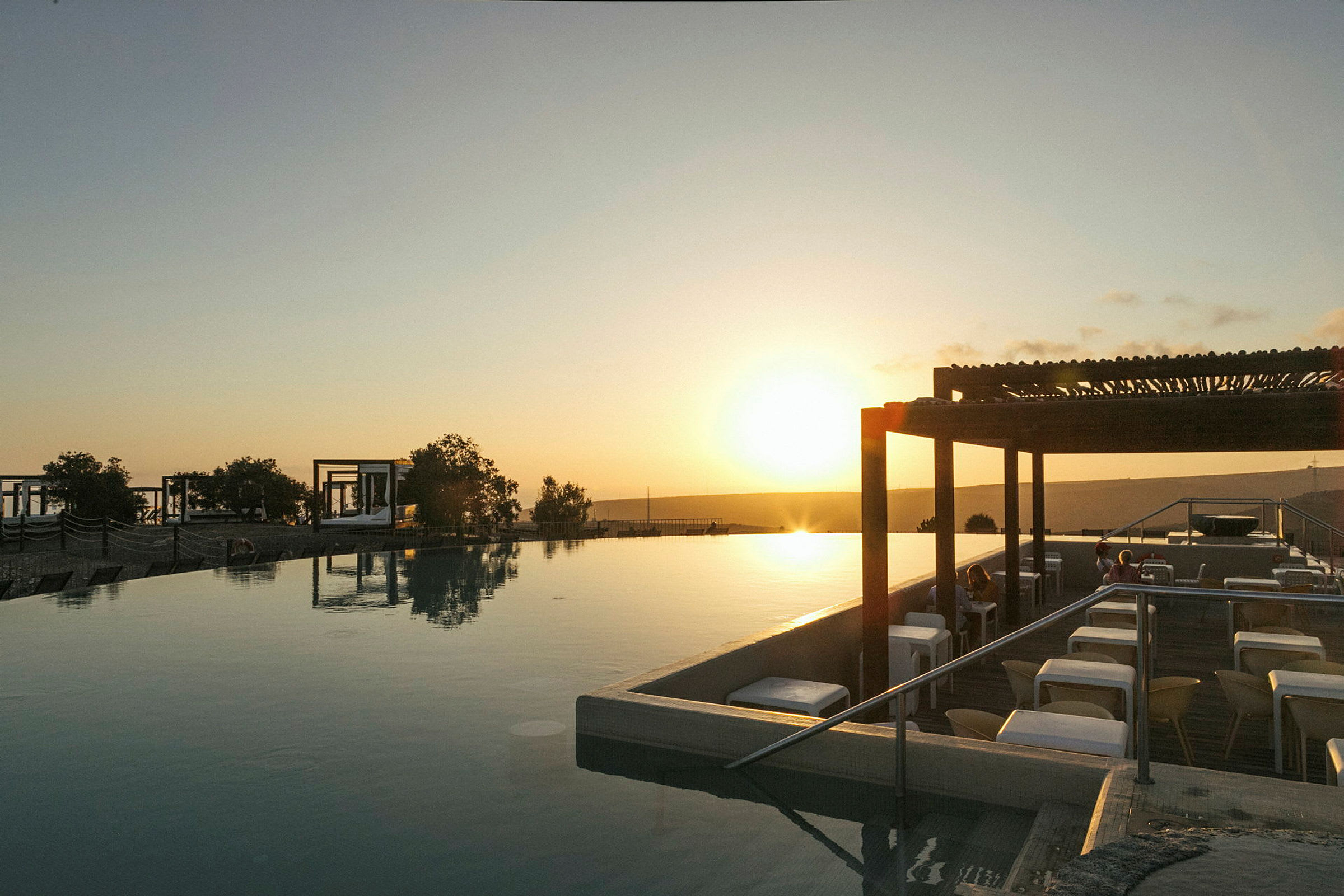 En solnedgang over en infinitypool med siddepladser ved siden af. (AI-genereret tekst)