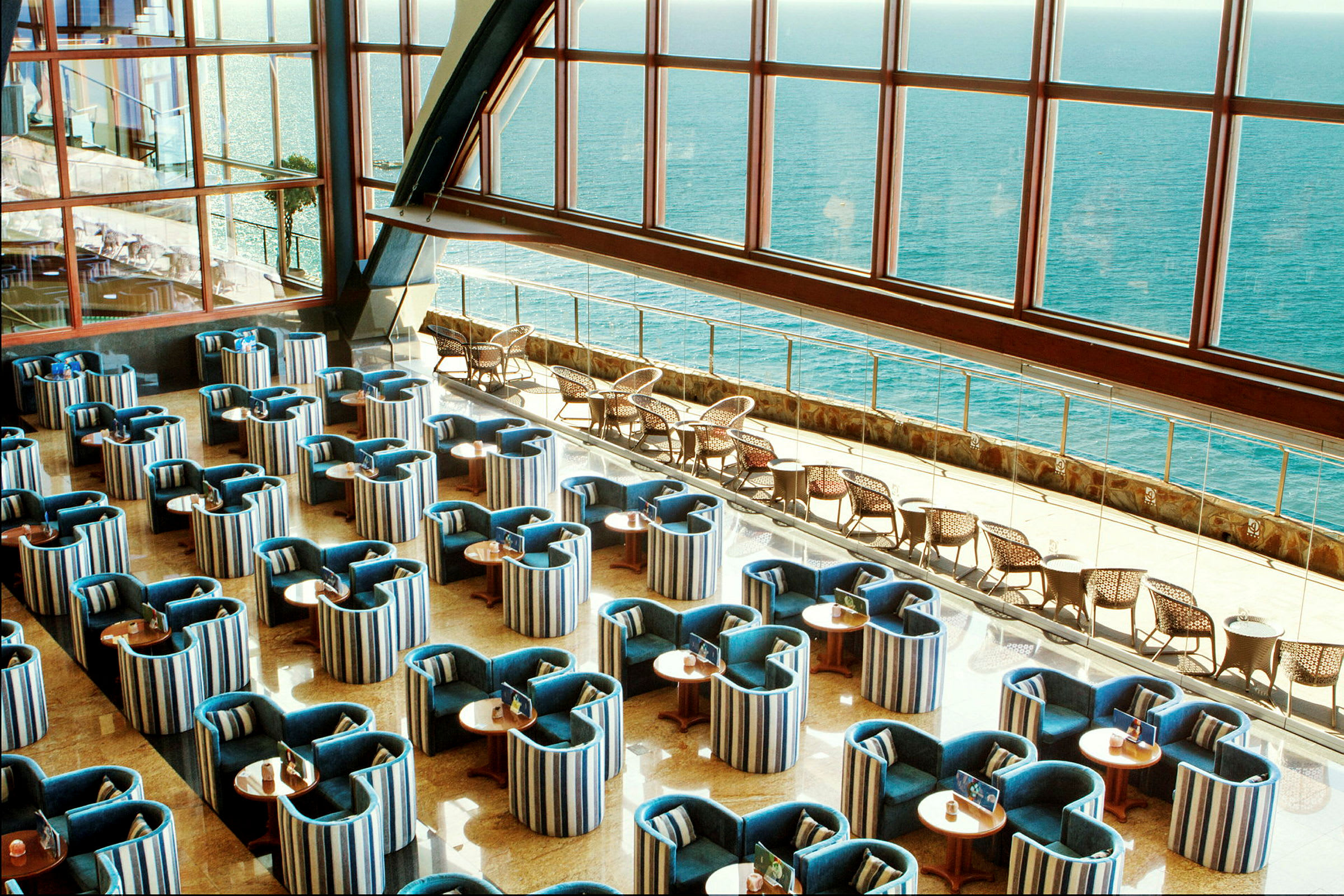 En indendørs lounge med organiserede siddepladser og stor vinduesudsigt over havet. (AI-genereret tekst)