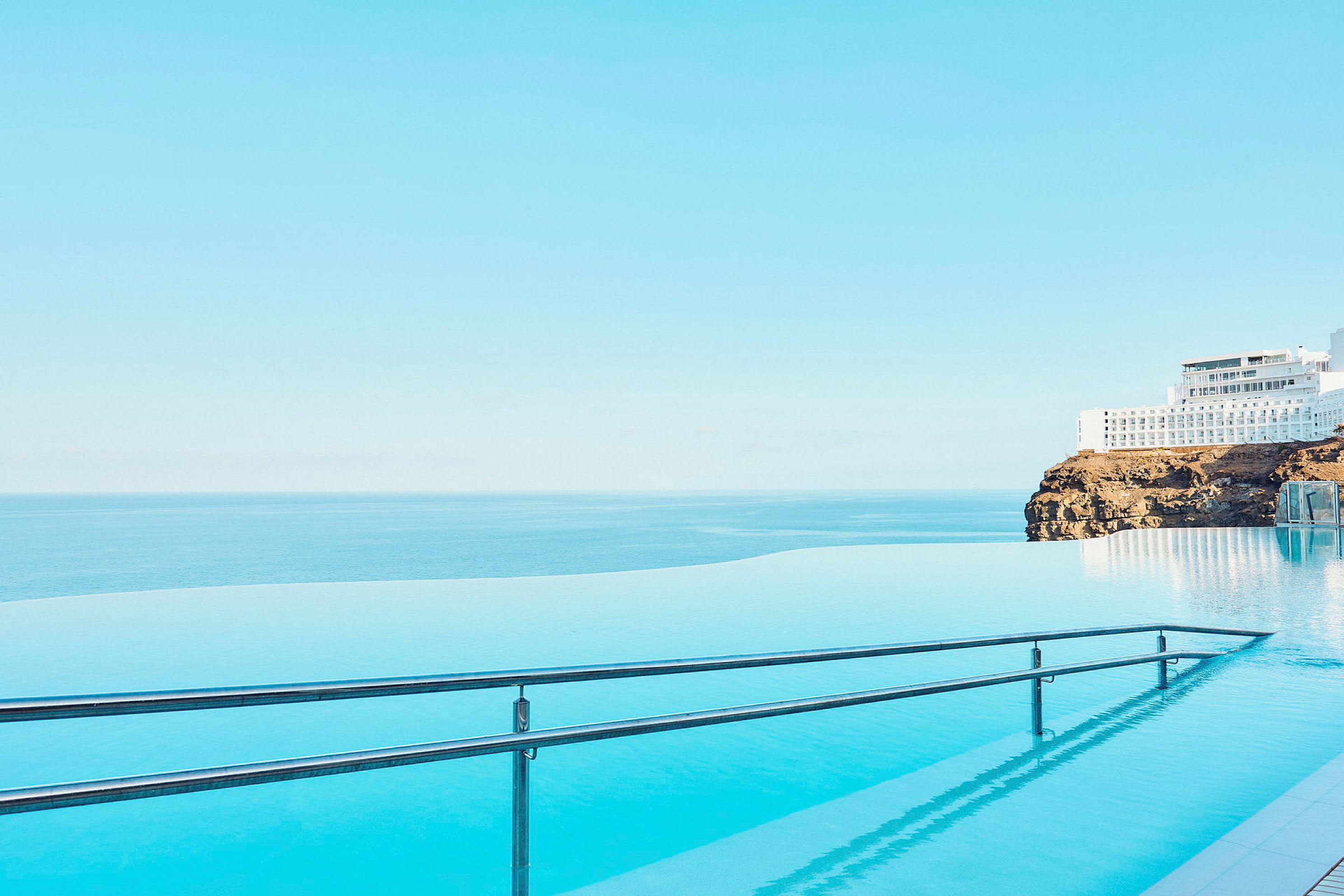 Infinitypool med udsigt over havet og en bygning på en klippe. (AI-genereret tekst)