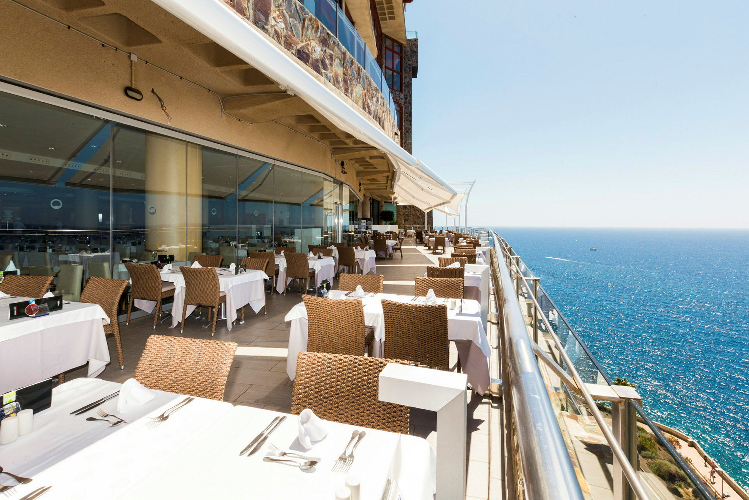 Restaurant med borde og stole på en terrasse med udsigt over havet. (AI-genereret tekst)