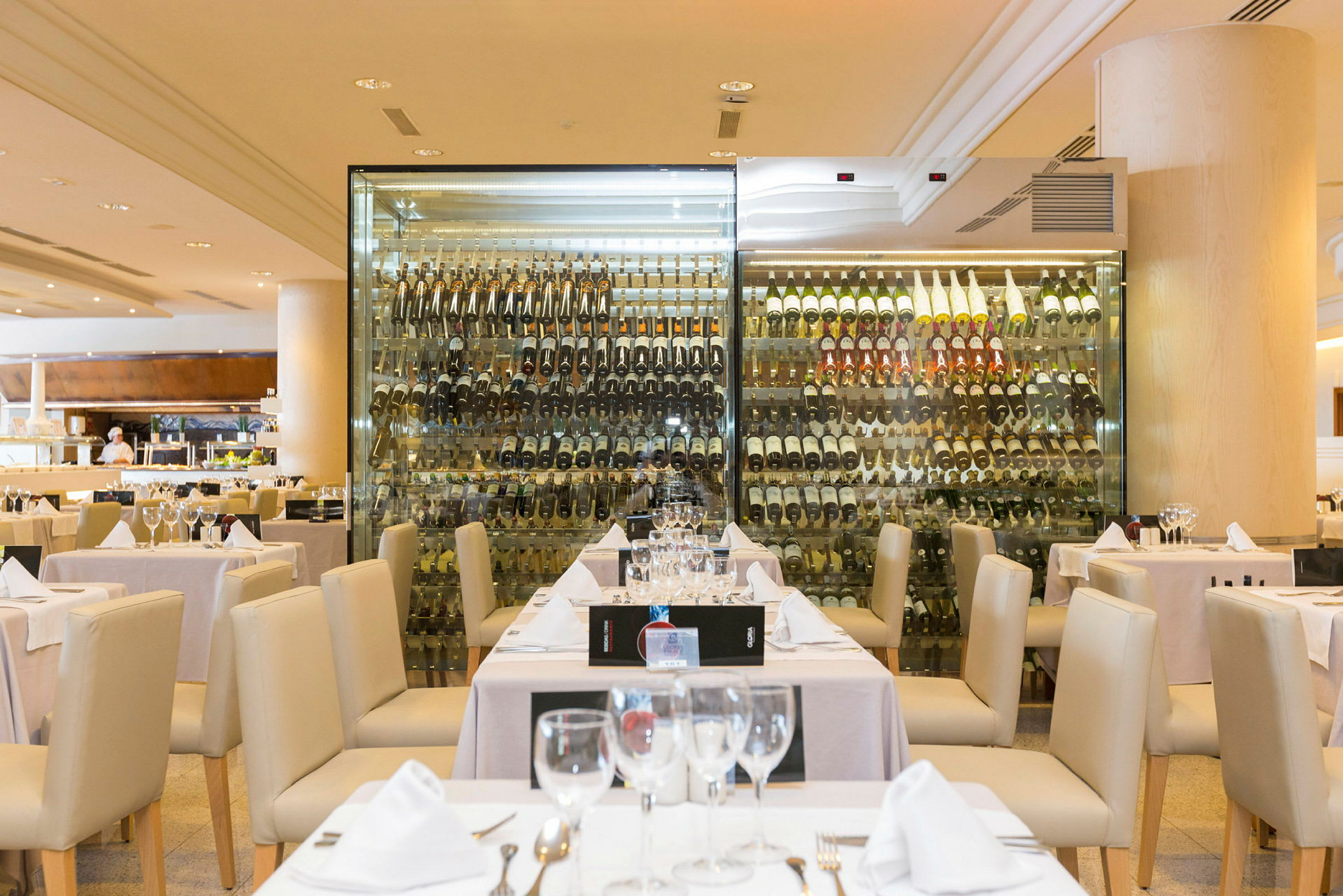 En restaurant med dækkede borde foran en glasvæg med en samling vinflasker. (AI-genereret tekst)