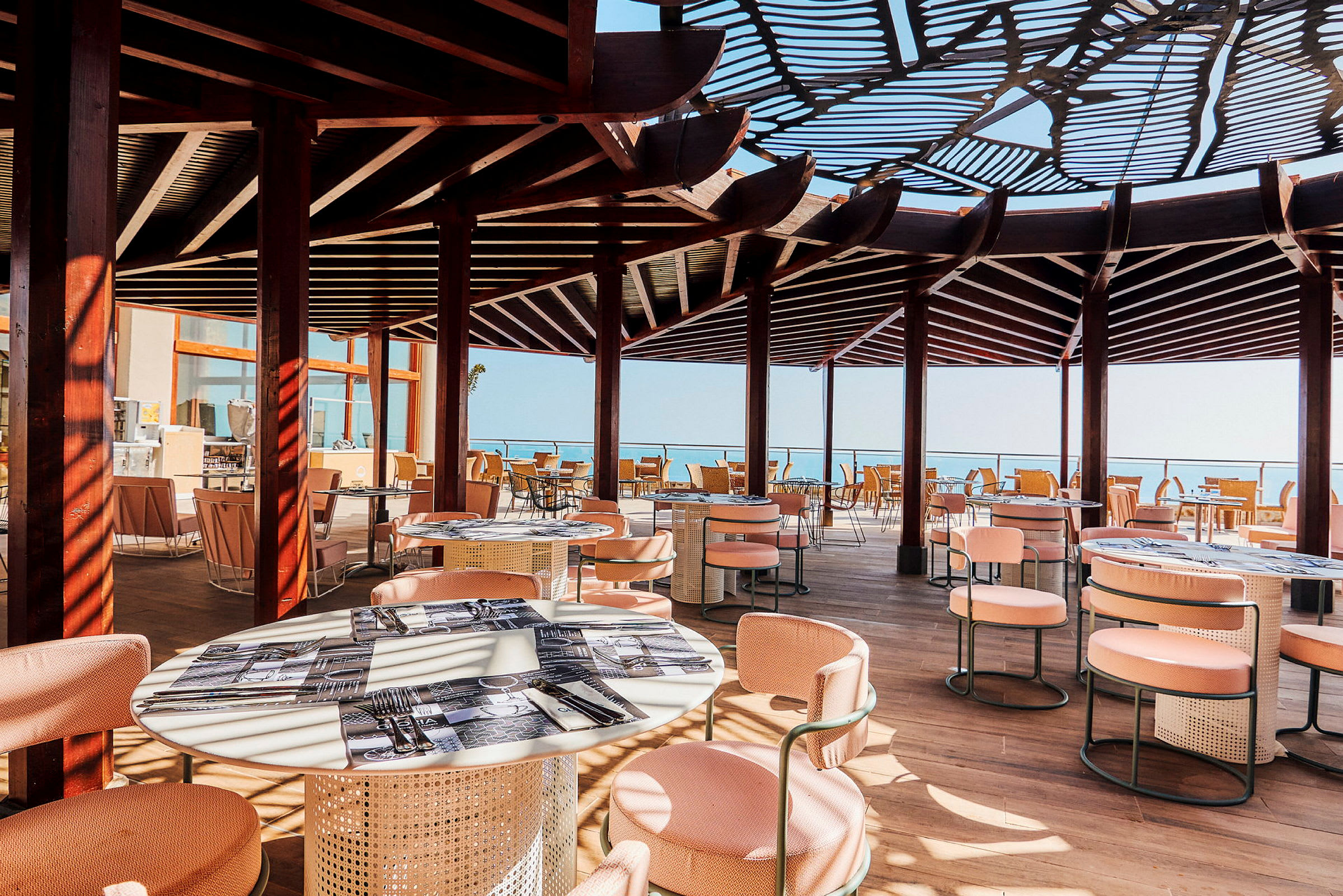 En udendørsrestaurant med skyggetag, borde og stole. Udsigt mod havet. (AI-genereret tekst)