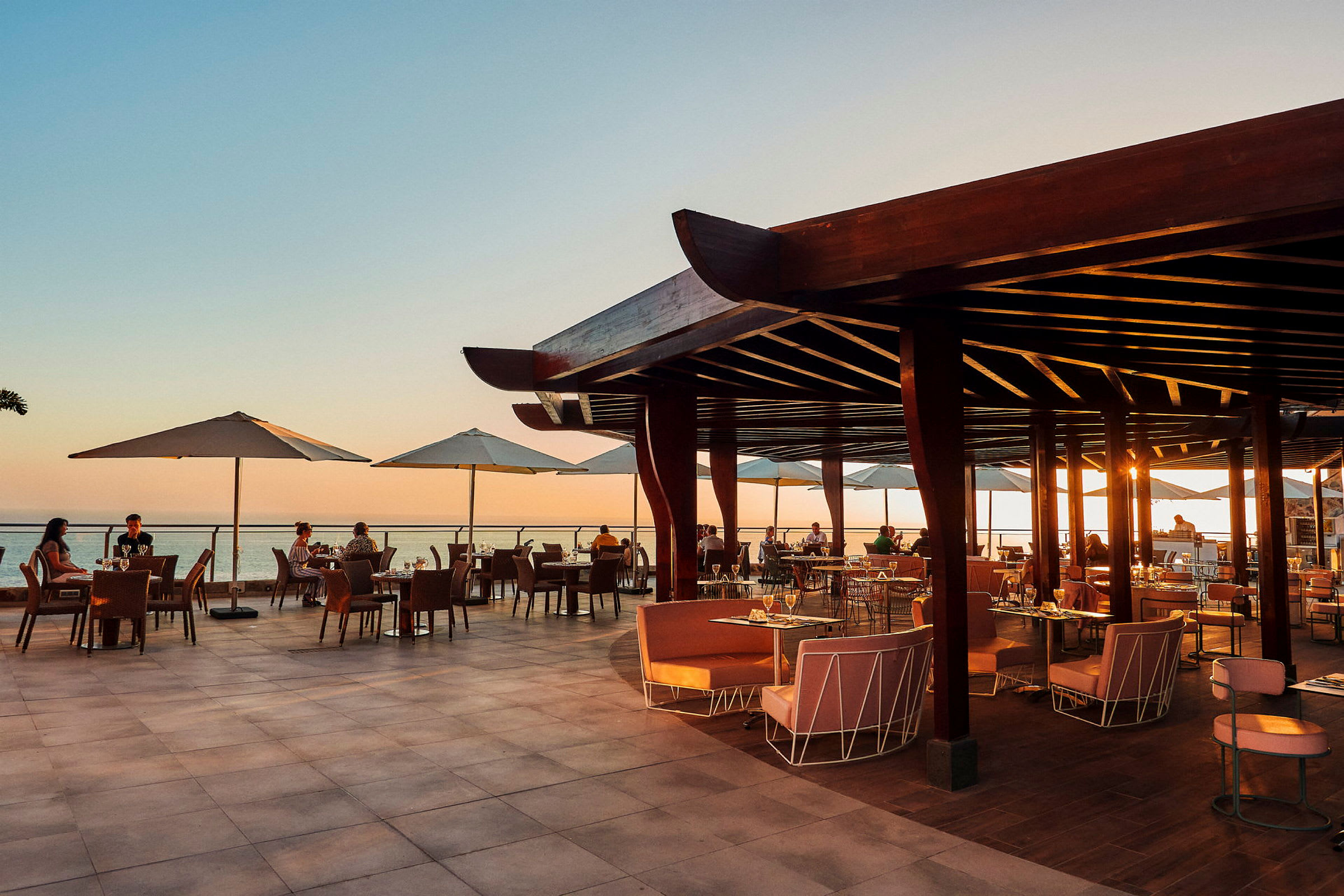 Åben restaurantterrasse med udsigt over havet ved solnedgang. (AI-genereret tekst)
