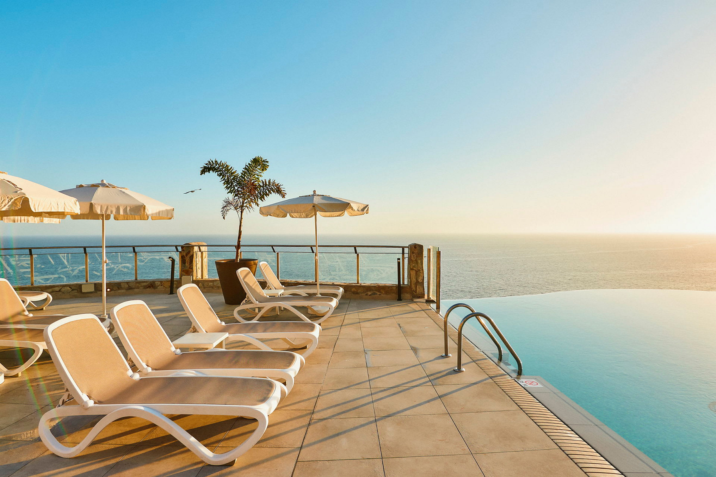 Liggestole og parasoller ved en infinitypool med udsigt over havet. (AI-genereret tekst)