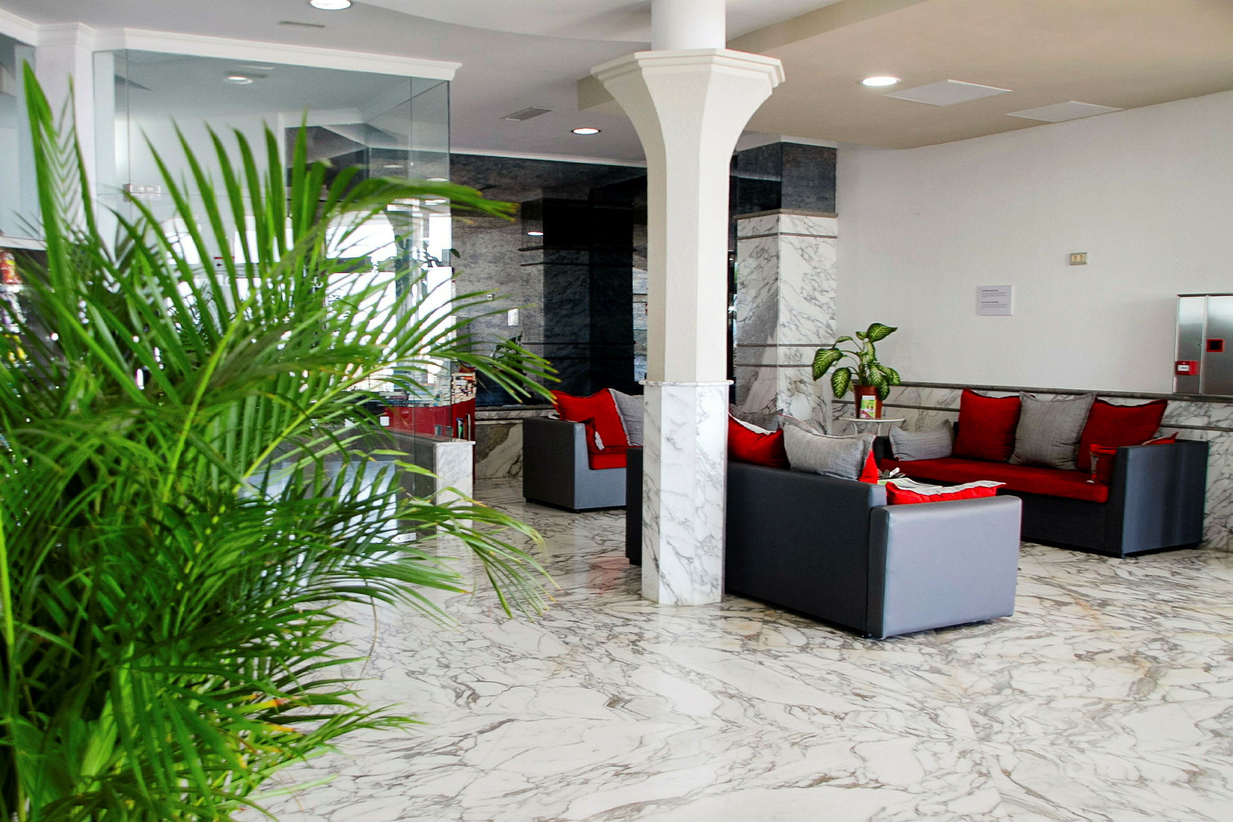 Lys og moderne lobby med marmorgulv, sofaer med røde puder og grøn plante. (AI-genereret tekst)