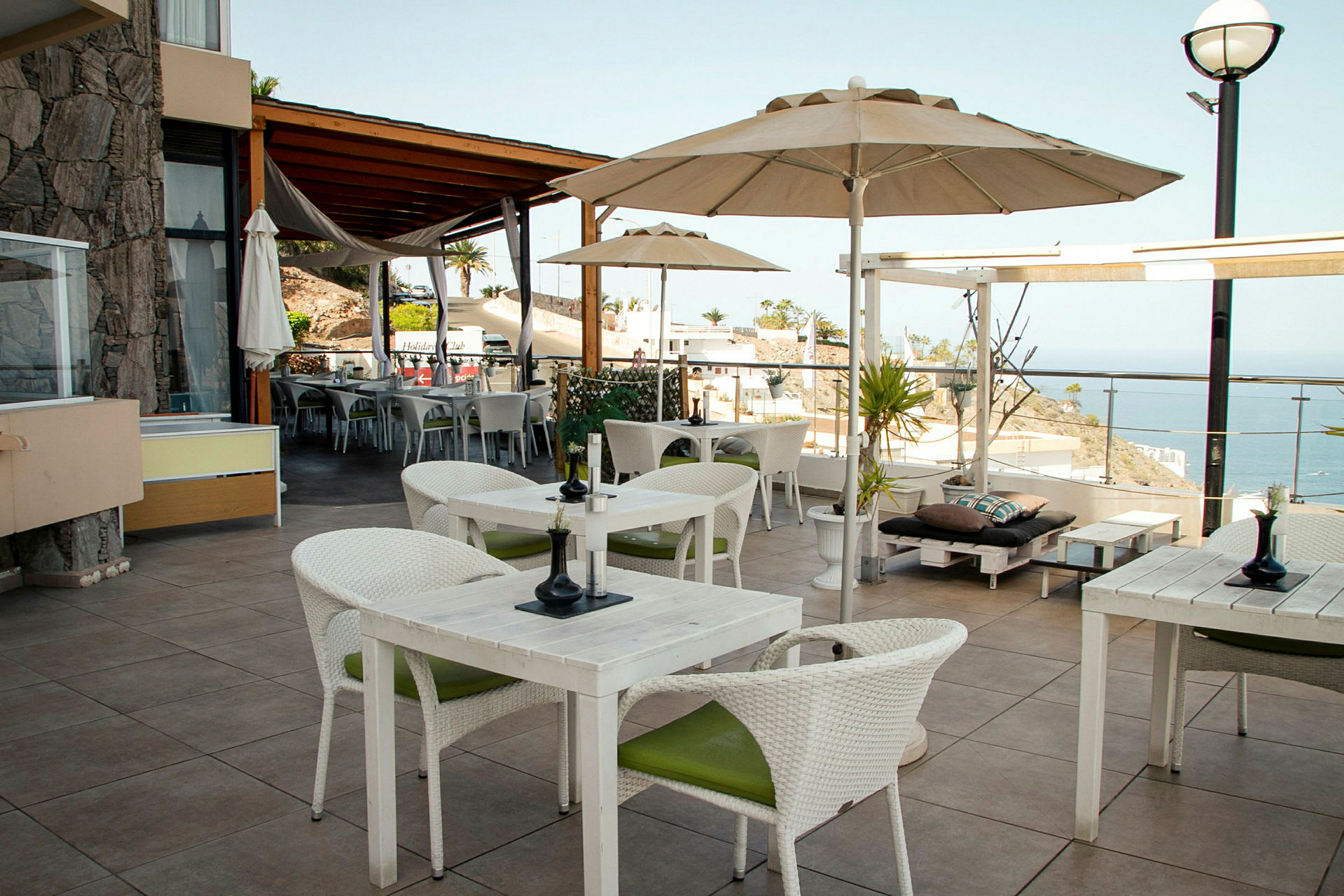 En terrasse med borde og stole samt udsigt over havet. (AI-genereret tekst)