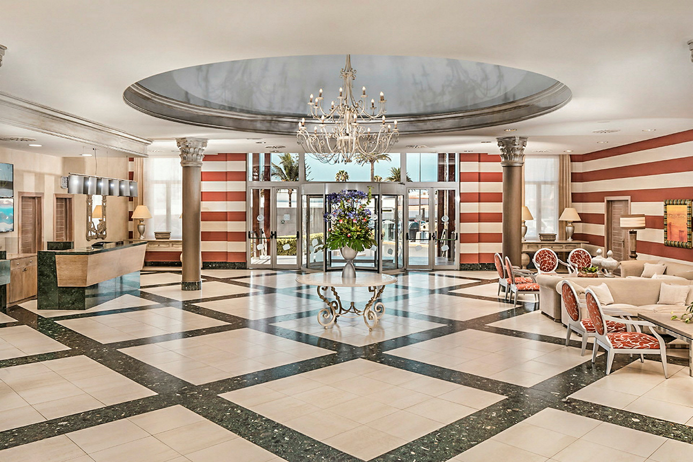 Et elegant hotellobbyområde med en lysekrone, marmorgulv, reception til venstre og siddepladser til højre. (AI-genereret tekst)