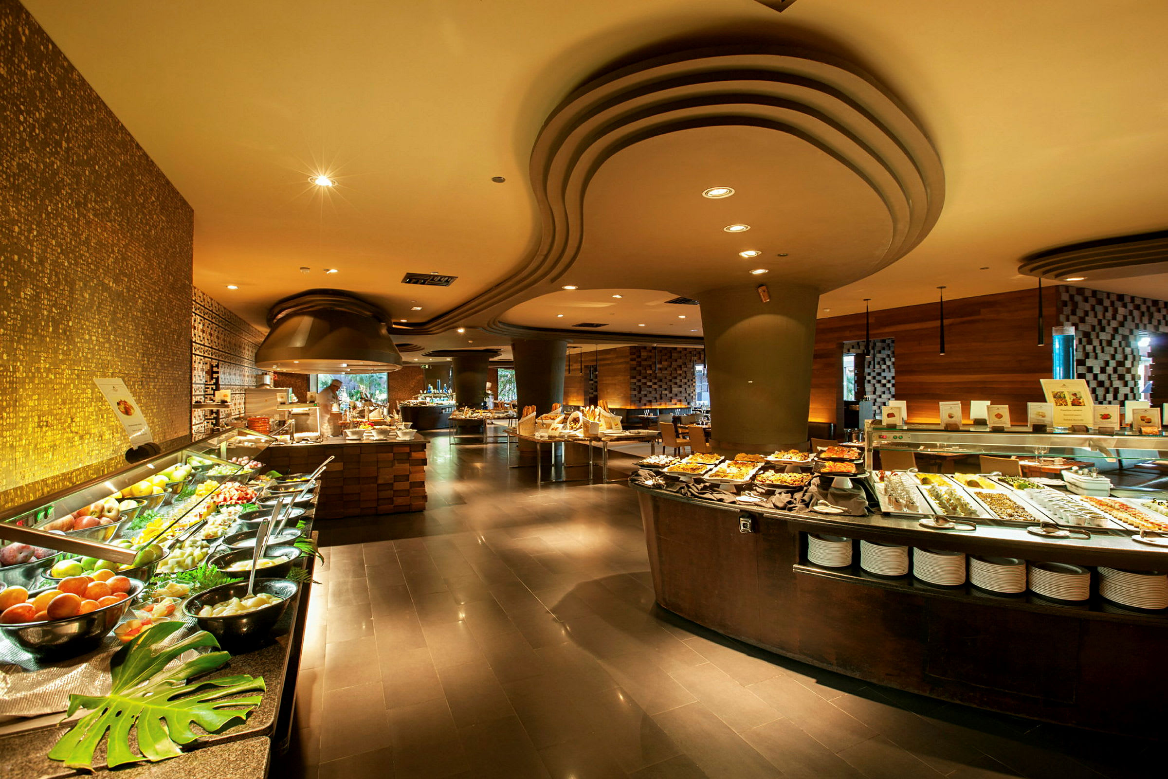En rummelig buffet med forskellige retter og salater på lange borde, omgivet af moderne interiør og stemningsfuld belysning. (AI-genereret tekst)