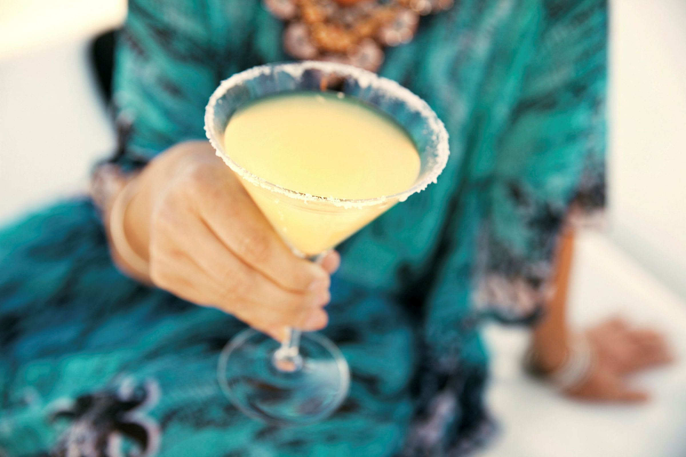 En person holder et cocktailglas fyldt med gul drikkelse og dekoreret med en sukkerkant. (AI-genereret tekst)