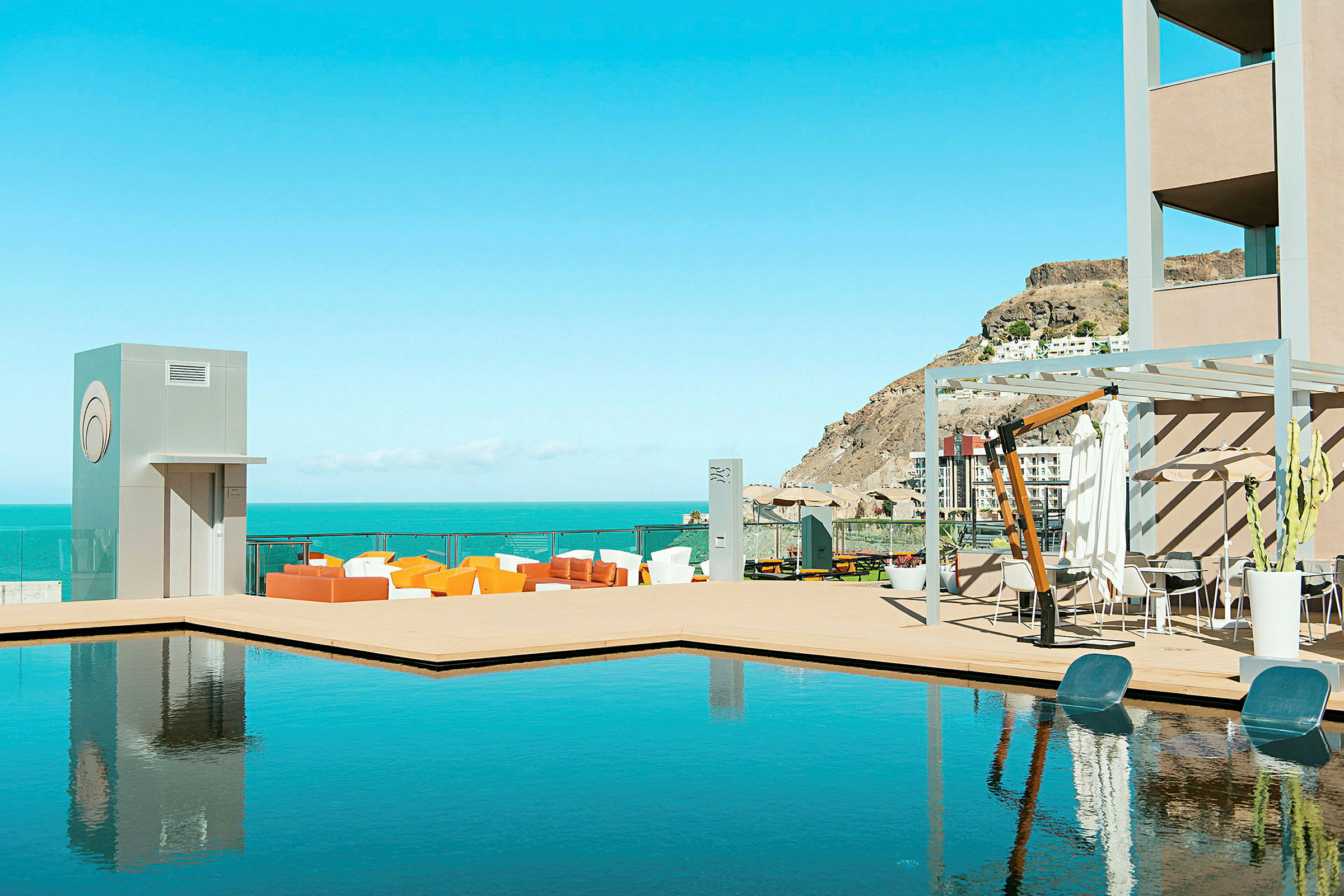 Billede der viser en terrasse med pool og siddepladser. Havet og bakker ses i baggrunden. (AI-genereret tekst)