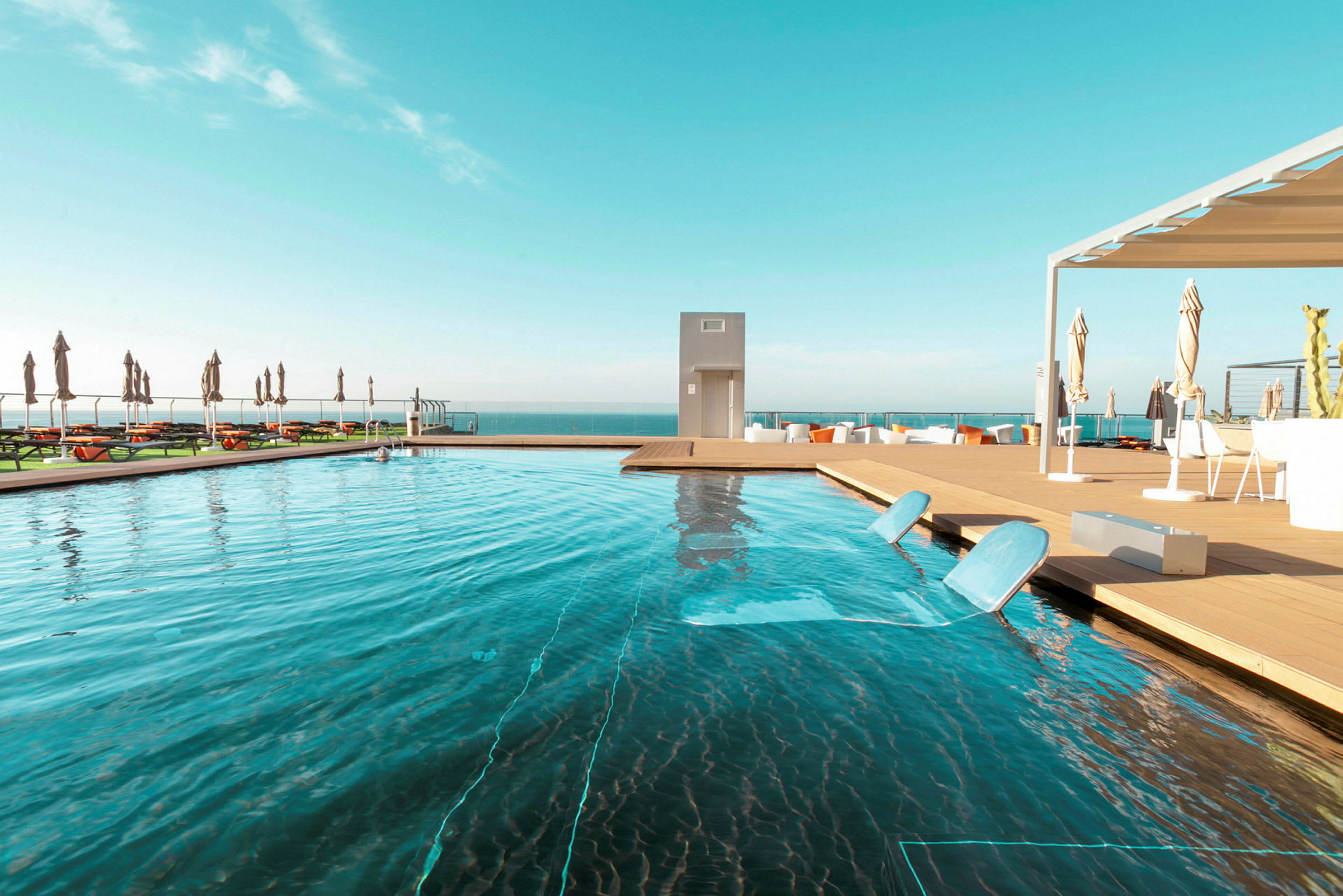 Udendørs swimmingpool med liggestole ved siden af og havet i baggrunden. (AI-genereret tekst)
