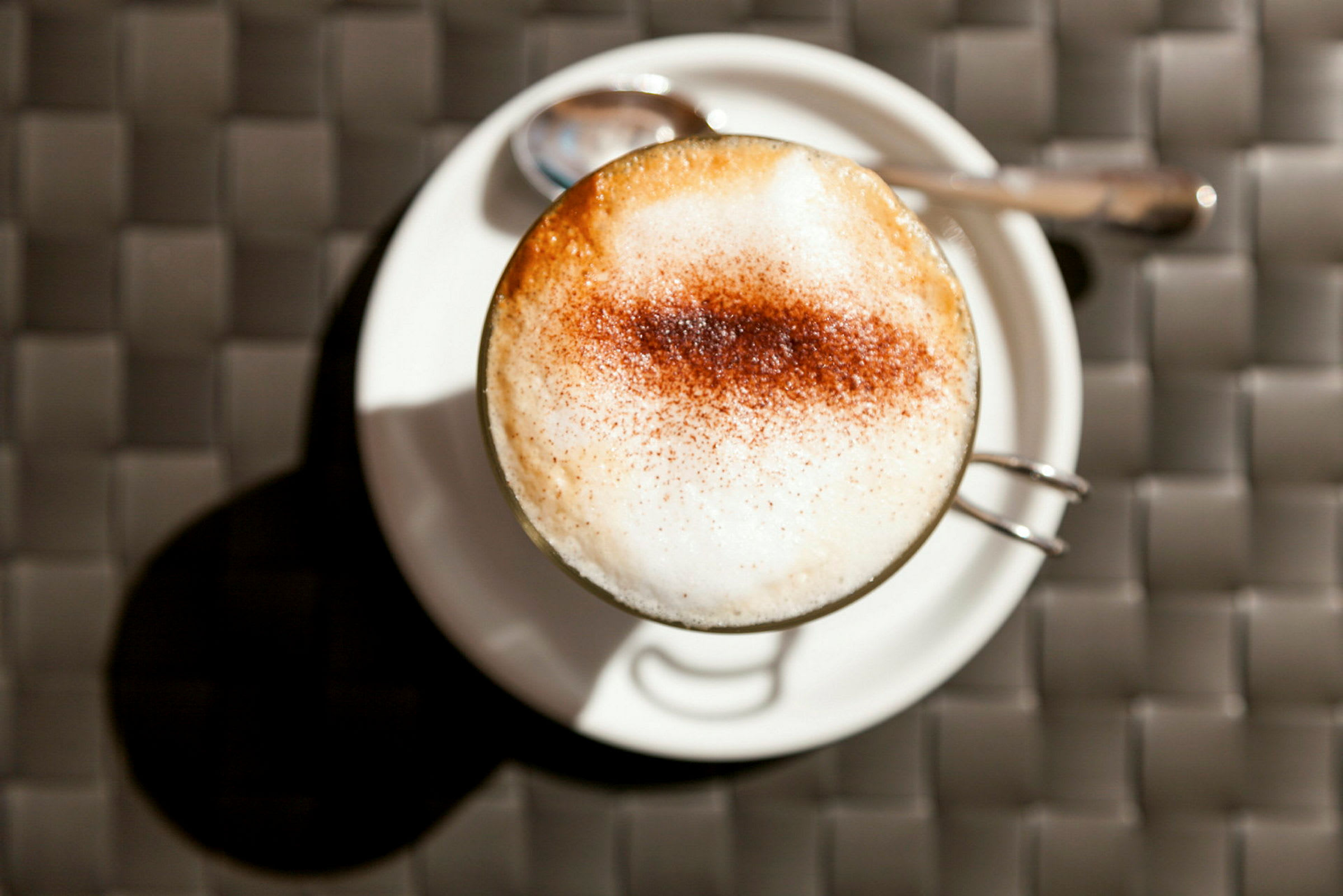 En kop cappuccino på en hvid tallerken med en ske ved siden af. (AI-genereret tekst)