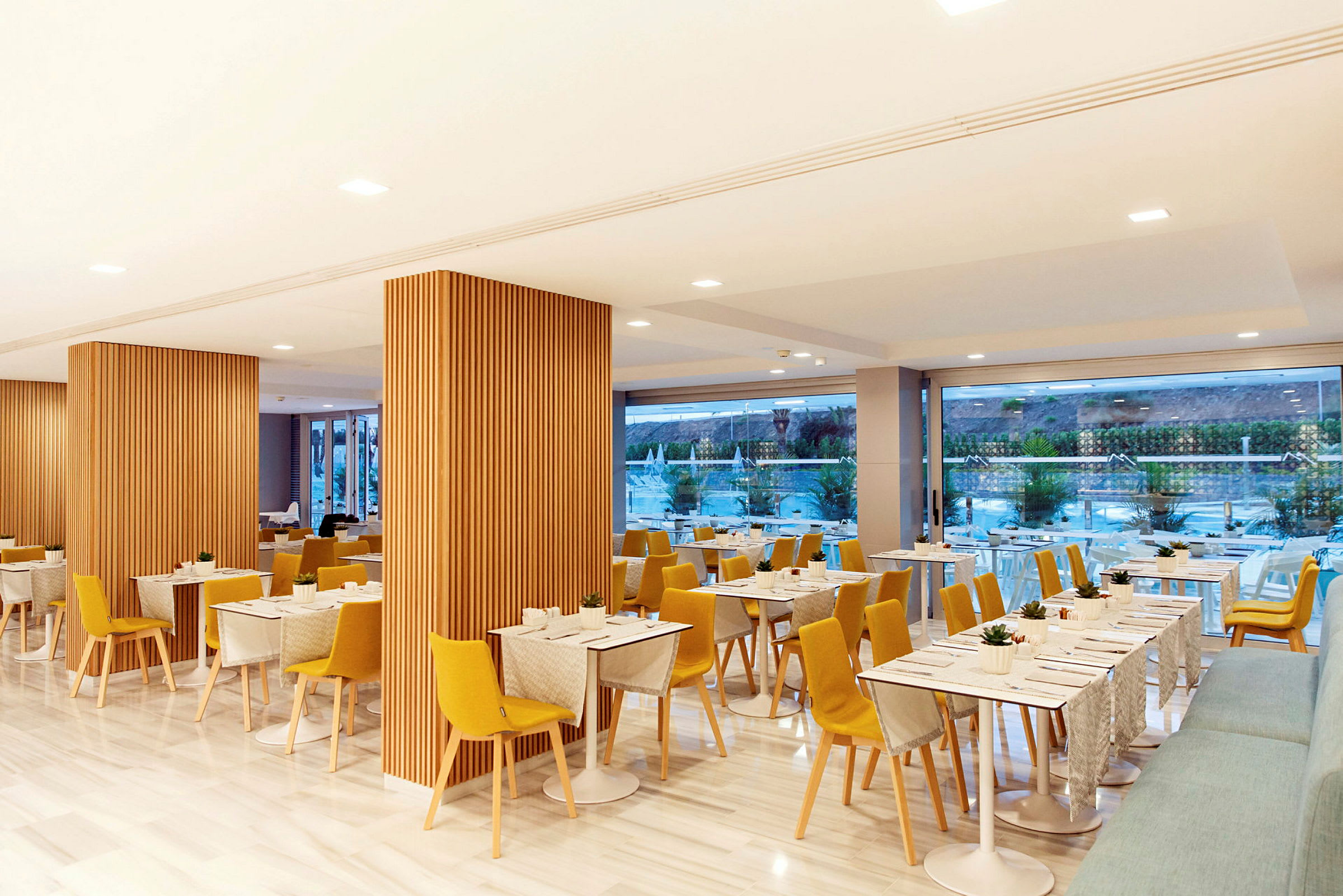 Billede af en moderne restaurant med trædekorationer, gule stole og borde med duge. (AI-genereret tekst)