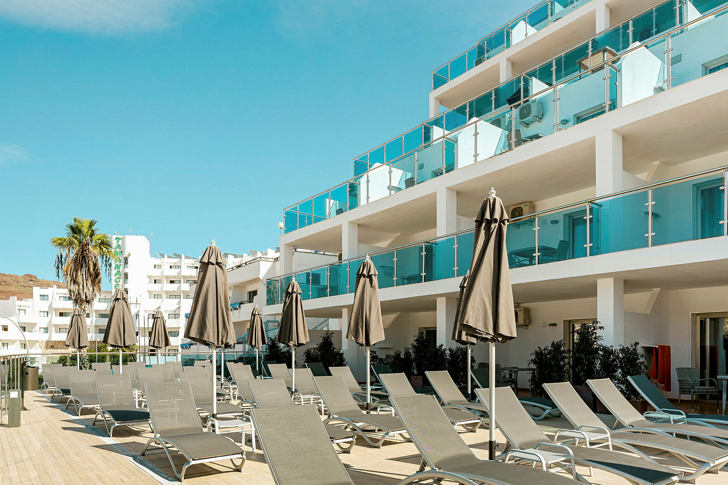 Billede af en hotelbygning med liggestole og parasoller på en terrasse. (AI-genereret tekst)