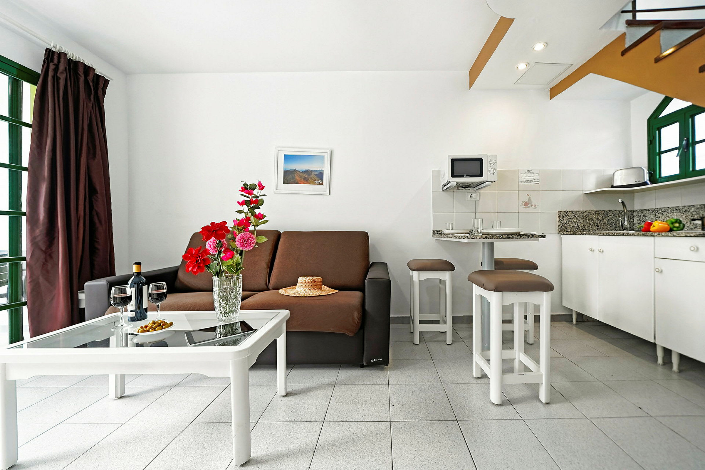 En stue med en sofa, kaffebord med blomster og et køkken i baggrunden. (AI-genereret tekst)