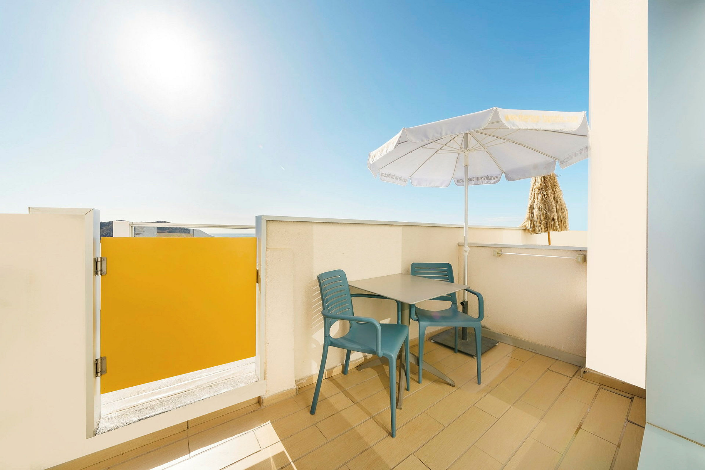 Billedet viser en terrasse med bord, to stole og en parasol. (AI-genereret tekst)