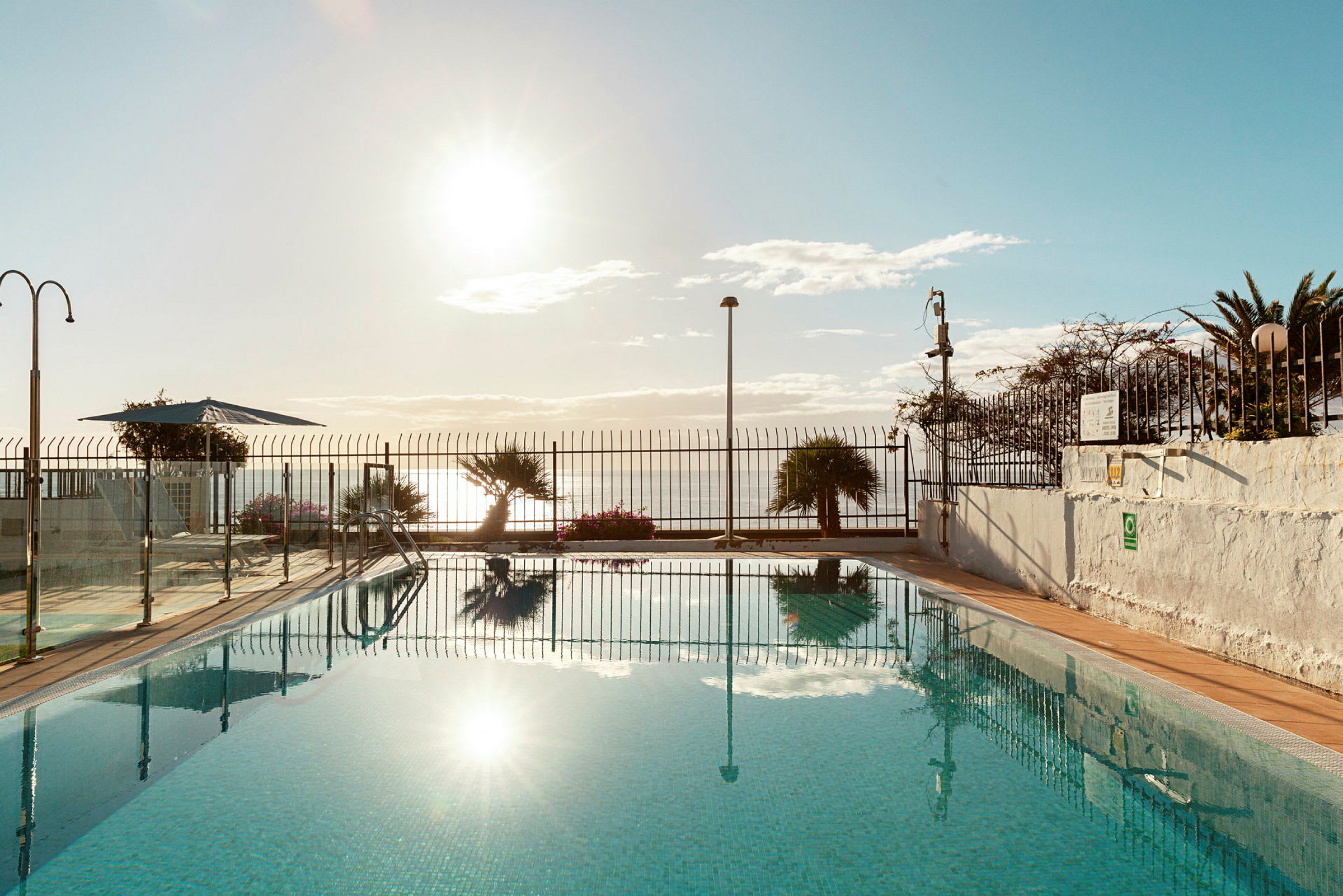 Udendørs swimmingpool med solnedgang i baggrunden. (AI-genereret tekst)