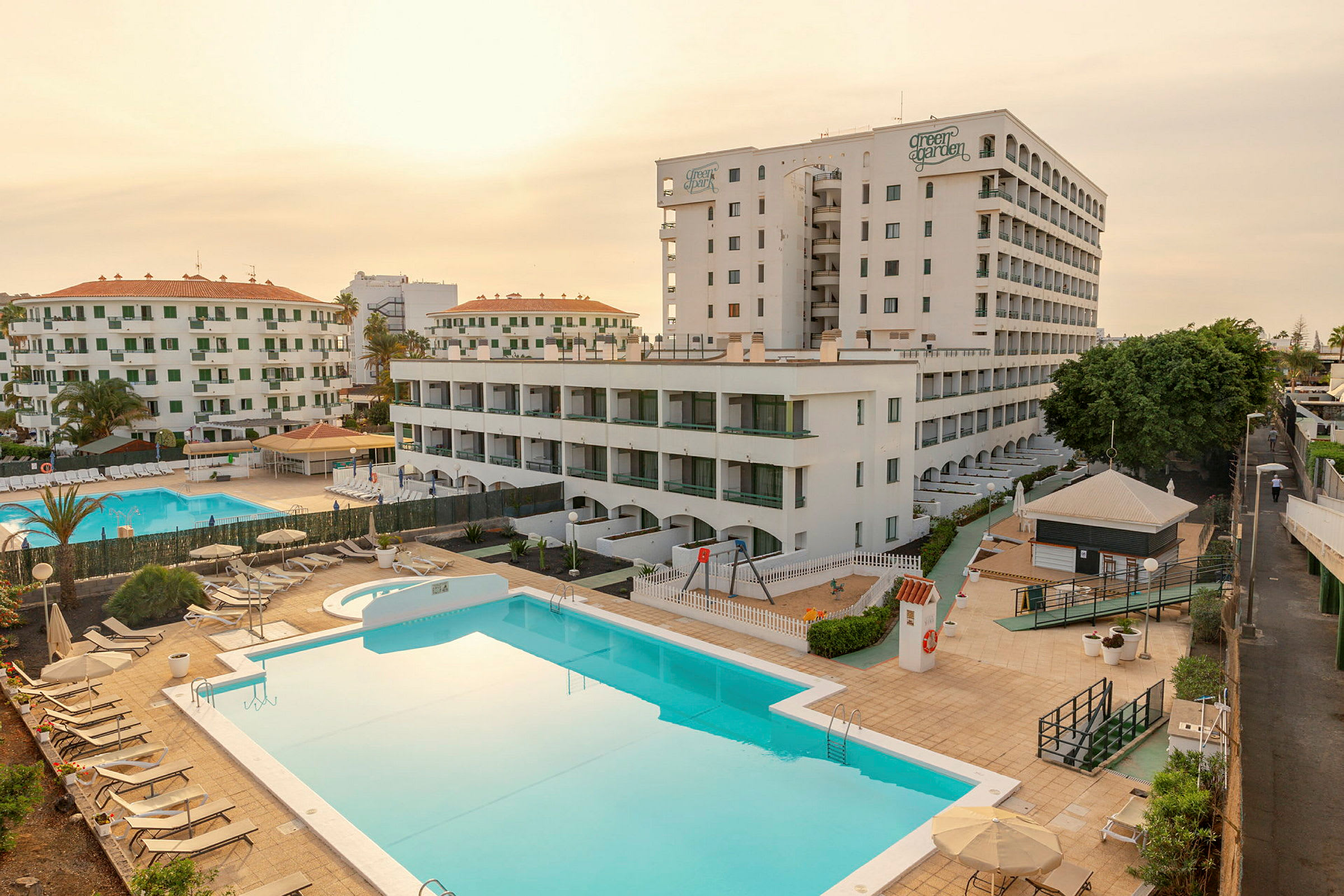 Et hotelkompleks med flere bygninger, to swimmingpools og liggestole. (AI-genereret tekst)