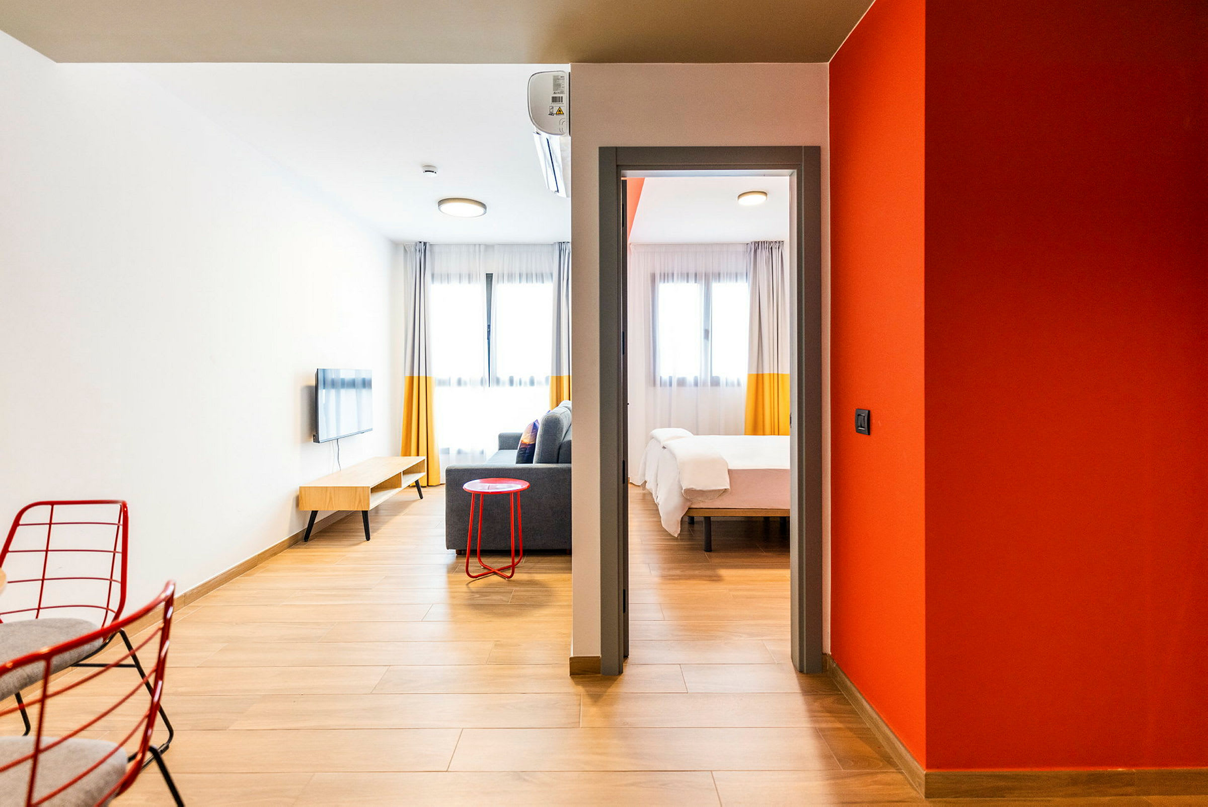 Et moderne hotelværelse med trægulv og indbydende indretning. Værelset har en siddegruppe med sofa, vægmonteret TV og et soveværelse med en dobbeltseng. (AI-genereret tekst)