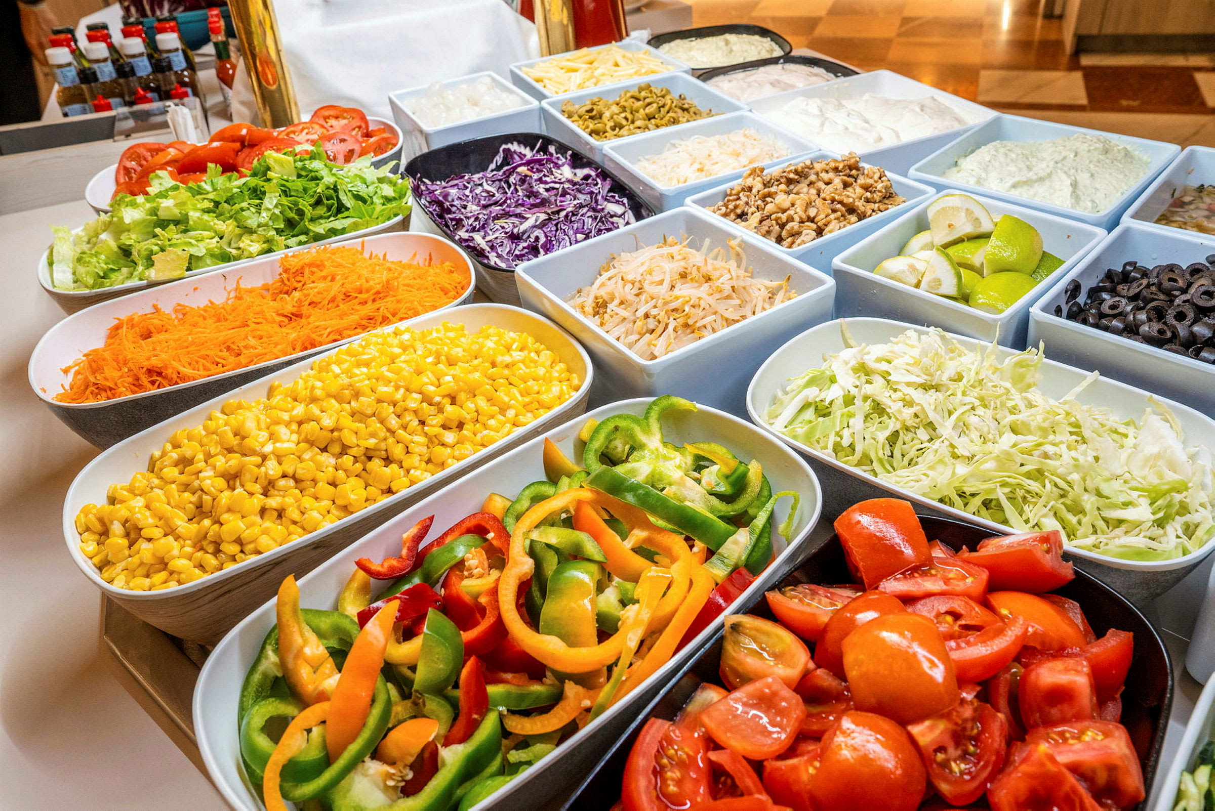 En buffet med forskellige grøntsager i skåle, herunder tomater, salat, majs, peberfrugt og oliven. (AI-genereret tekst)