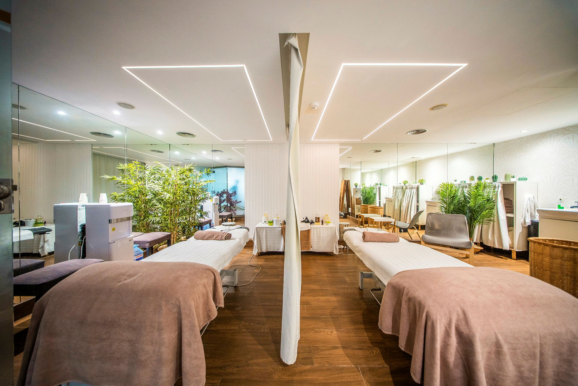 Et spa-rum med to massageborde, dekoreret med planter og spejle. (AI-genereret tekst)