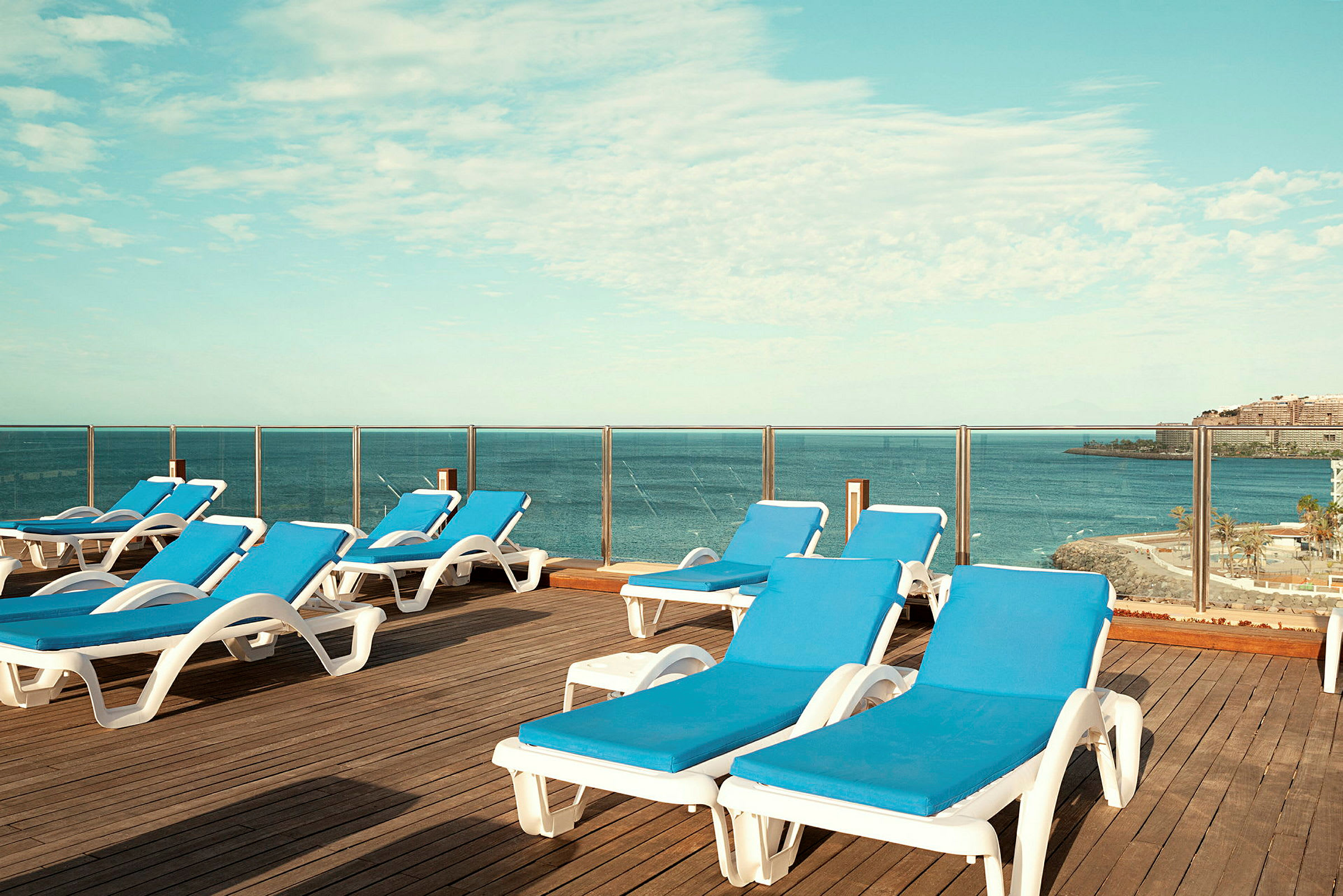 Liggestole med blå puder på en terrasse med udsigt over havet. (AI-genereret tekst)
