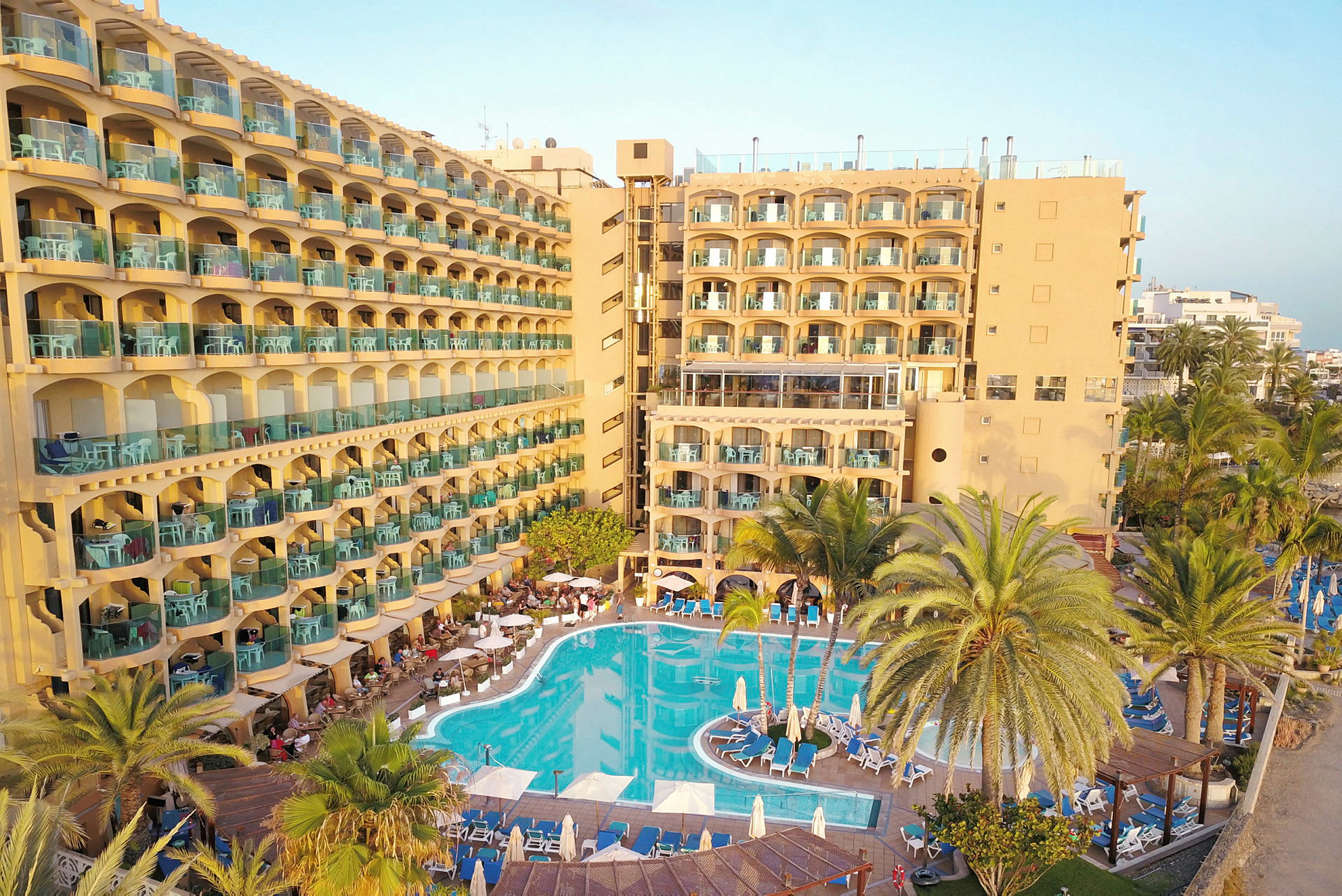 Hotel med gul facade, altaner og swimmingpool. (AI-genereret tekst)