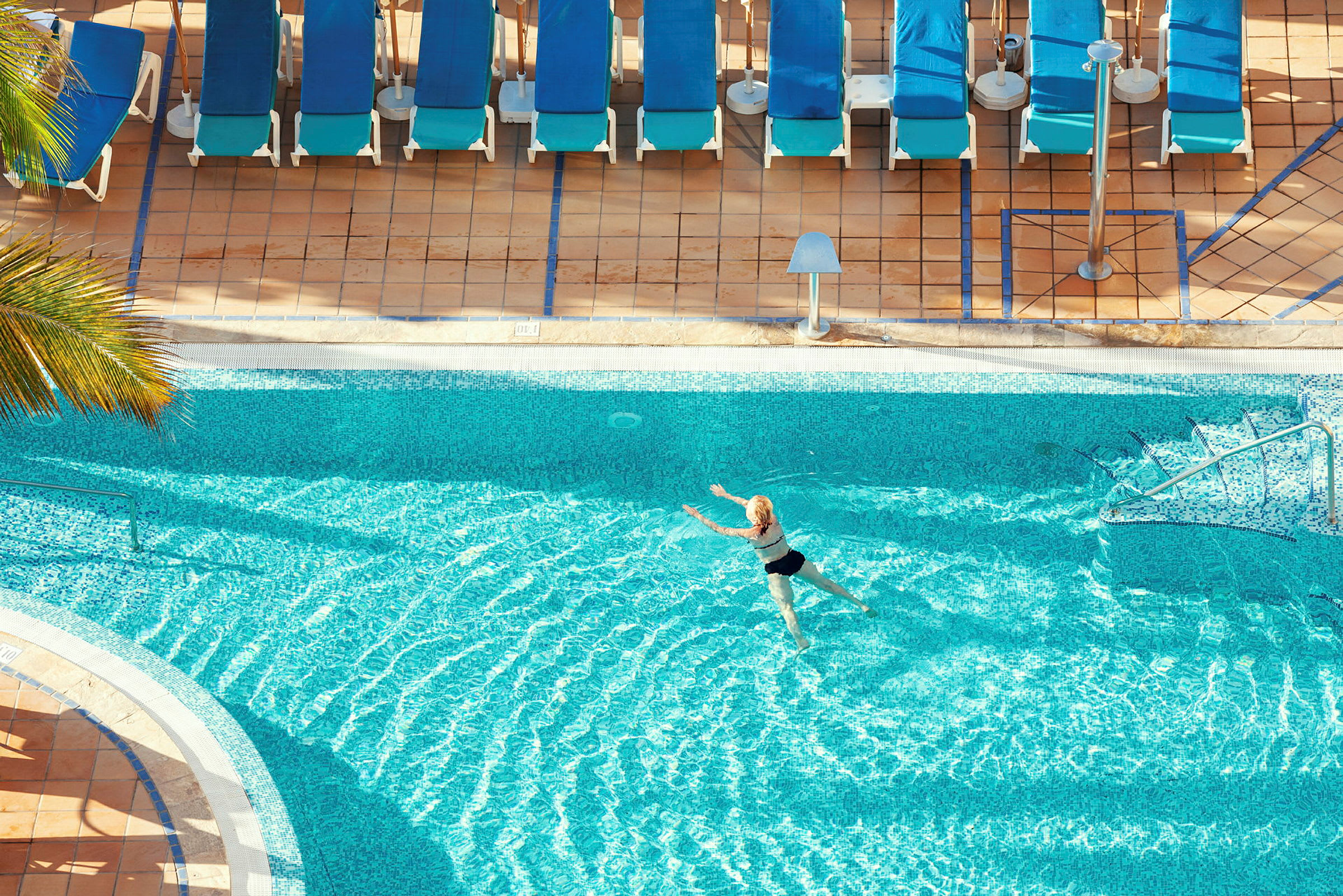 En person svømmer i en pool tæt på flere liggestole. (AI-genereret tekst)