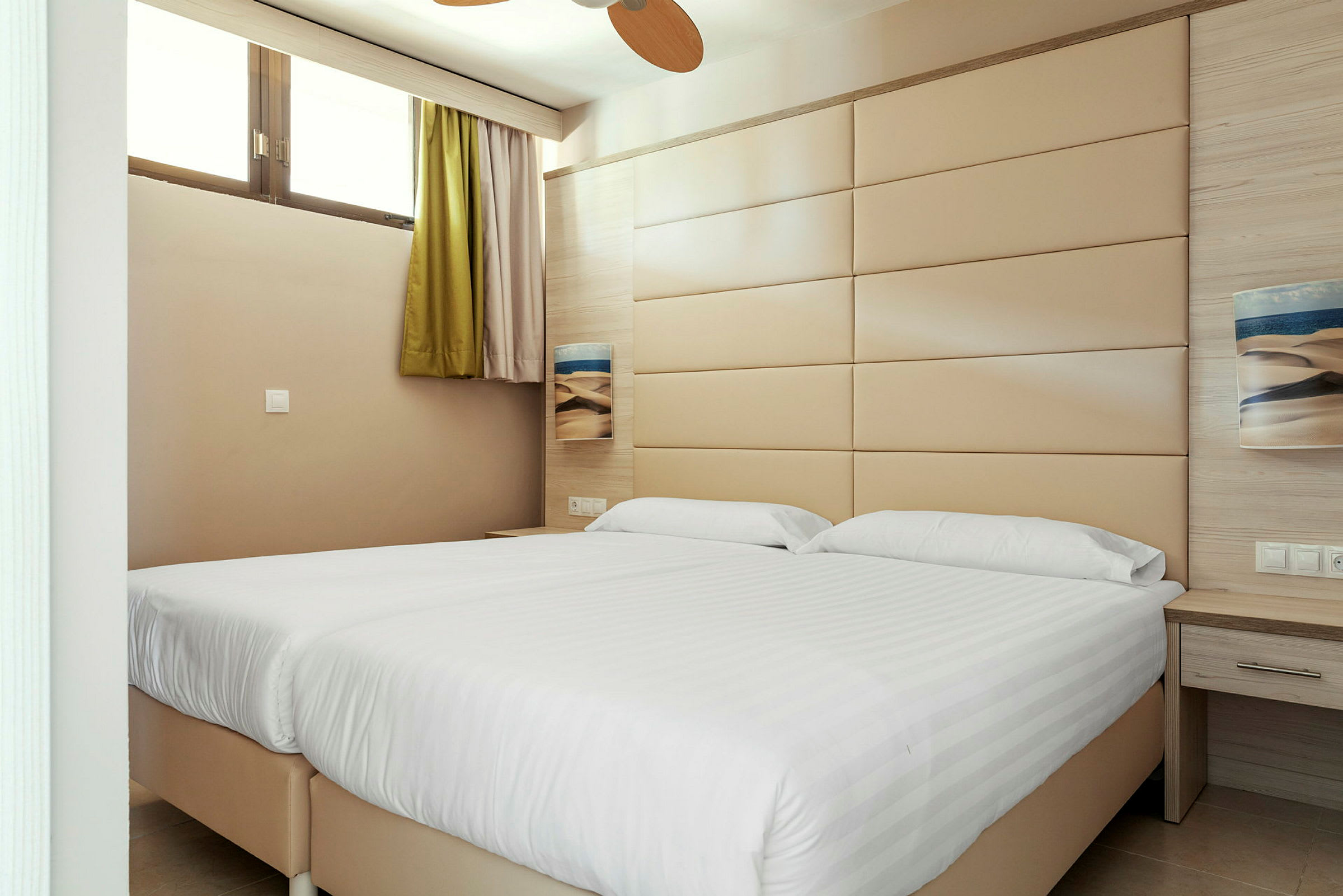 Et hotelværelse med to senge og en beige vægpanel. (AI-genereret tekst)