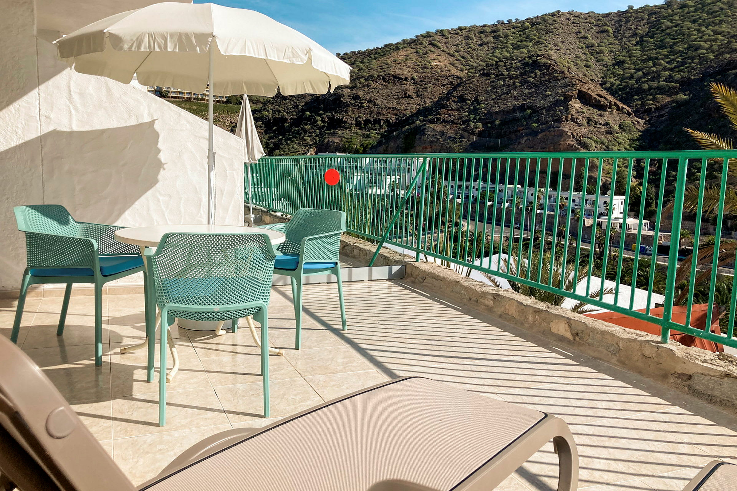 Terrasse med bord, stole og parasol, bjerge i baggrunden. (AI-genereret tekst)