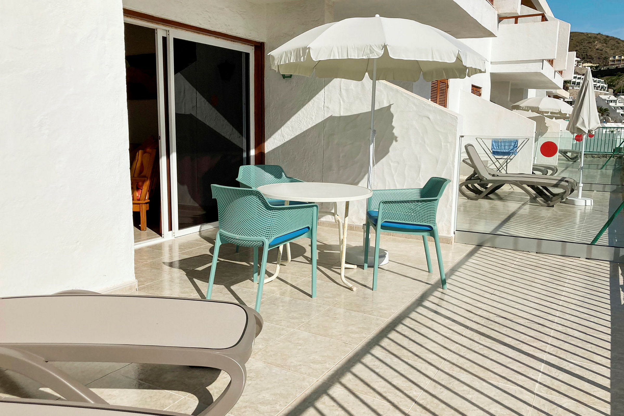 Billedet viser en terrasse med bord og stole under en parasol. (AI-genereret tekst)