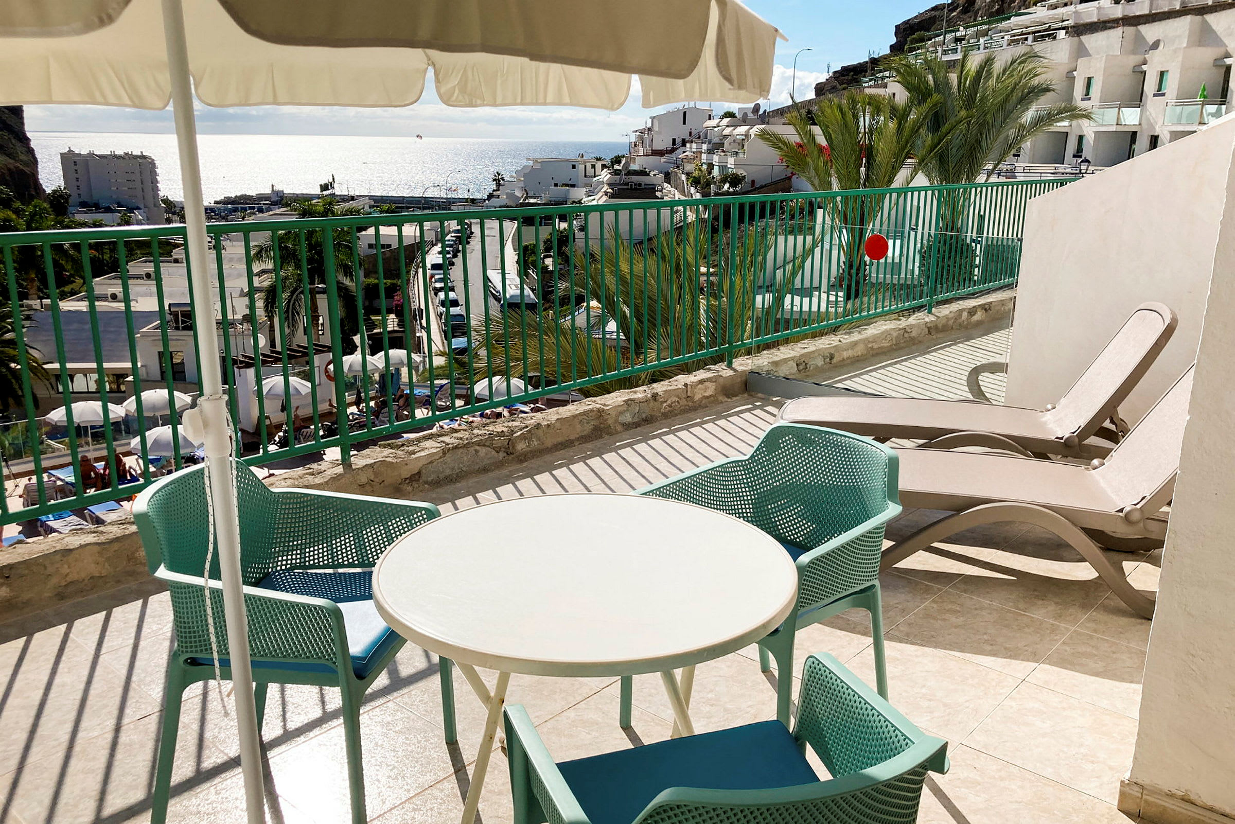 Terrasse med et rundt bord, stole og solsenge, havudsigt i baggrunden. (AI-genereret tekst)