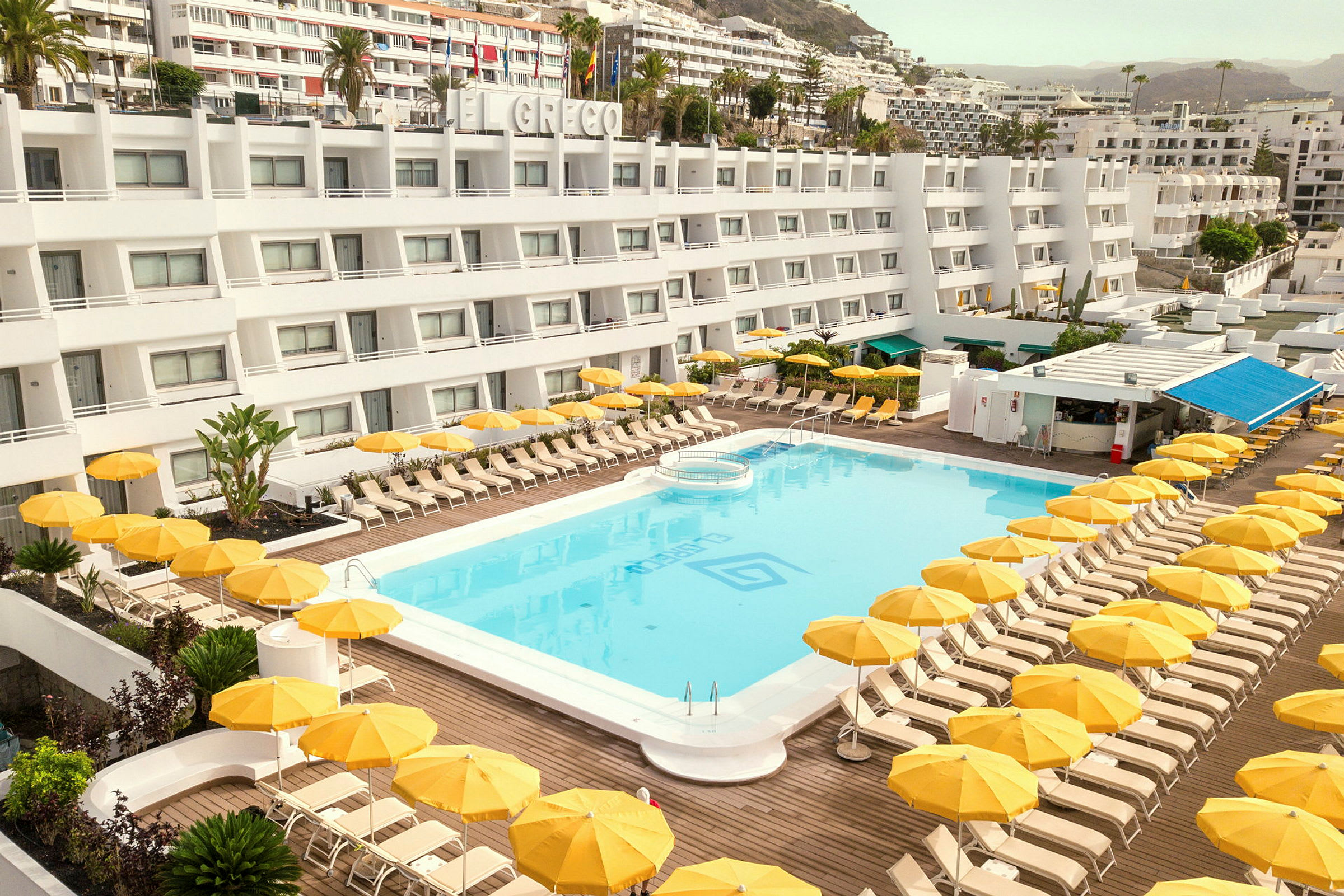 Hotel med pool og gule parasoller. (AI-genereret tekst)