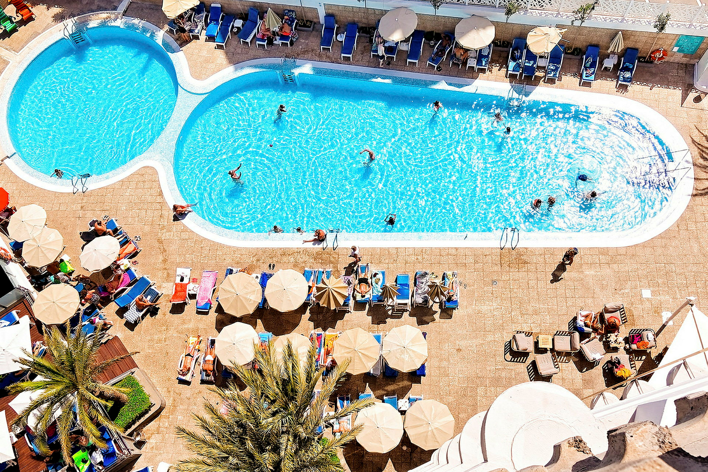 En udendørs swimmingpool med liggestole og parasoller ved siden af. (AI-genereret tekst)