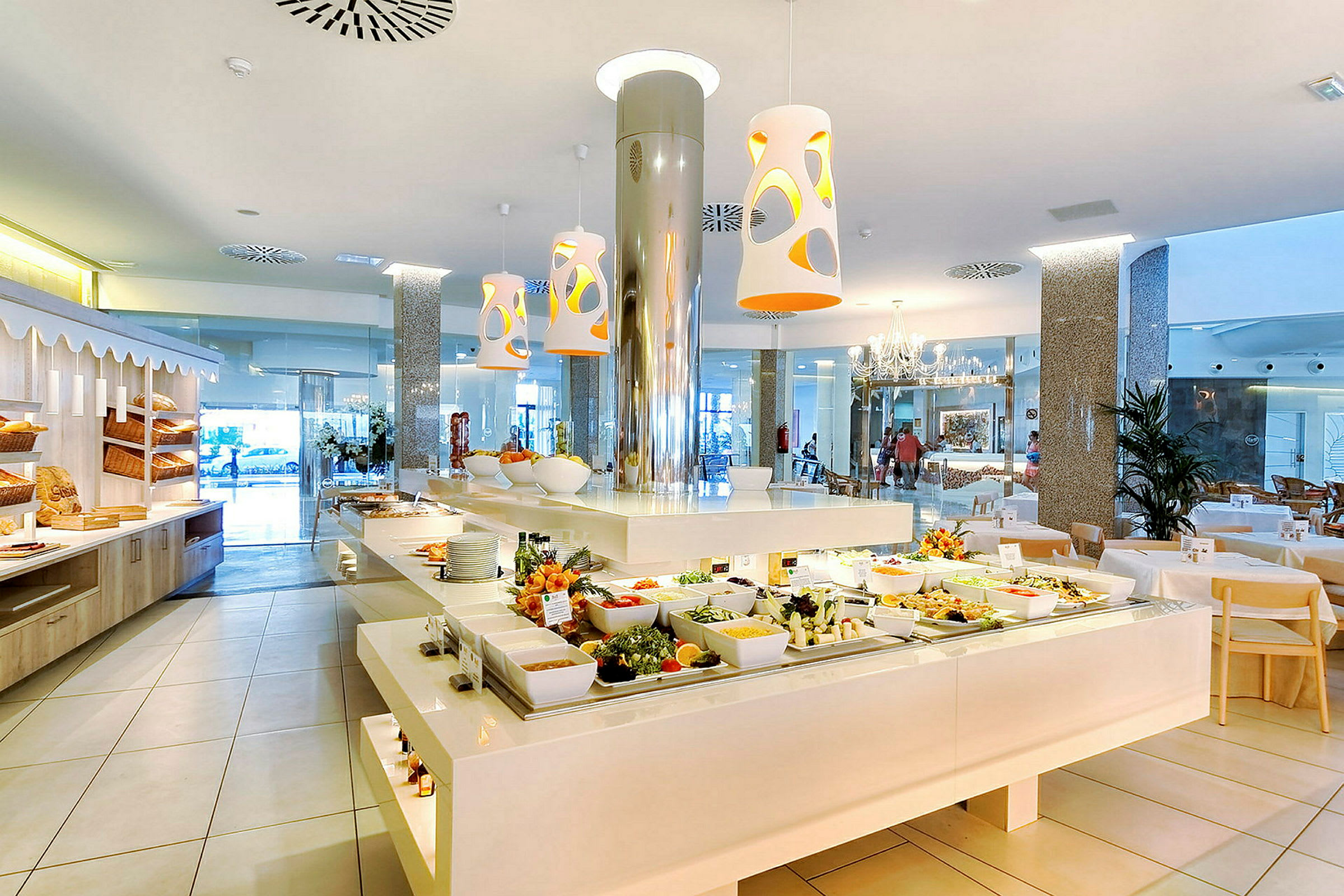 En lys restaurant med en buffetbord fyldt med forskellige retter og salatingredienser. Moderne indretning og store vinduer i baggrunden. (AI-genereret tekst)