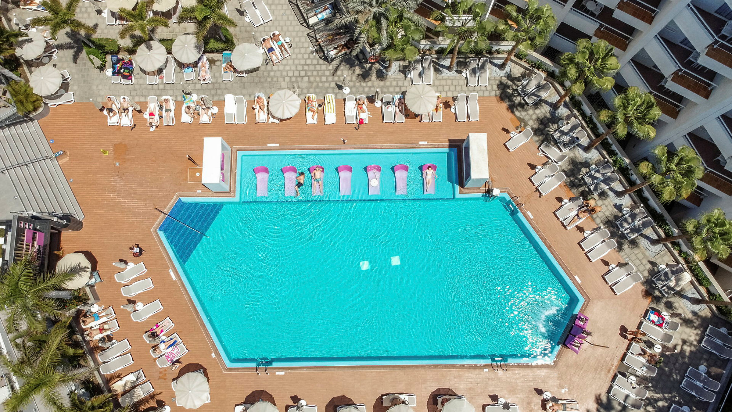 Luftfoto af en swimmingpool omgivet af liggestole og parasoller. (AI-genereret tekst)