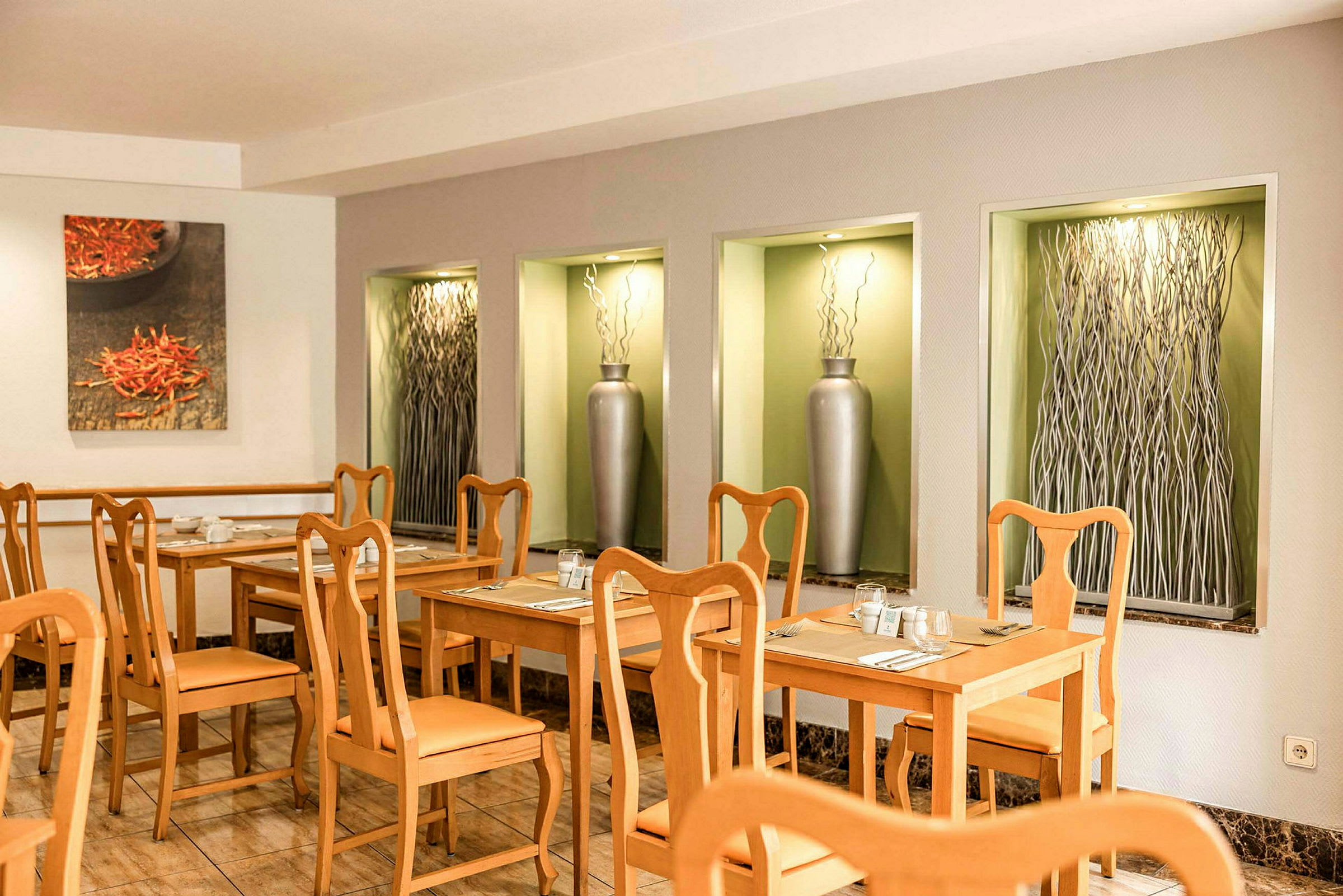Et restaurantområde med træborde og stole samt dekorative åbninger i væggen med vaser og kunstværker. (AI-genereret tekst)