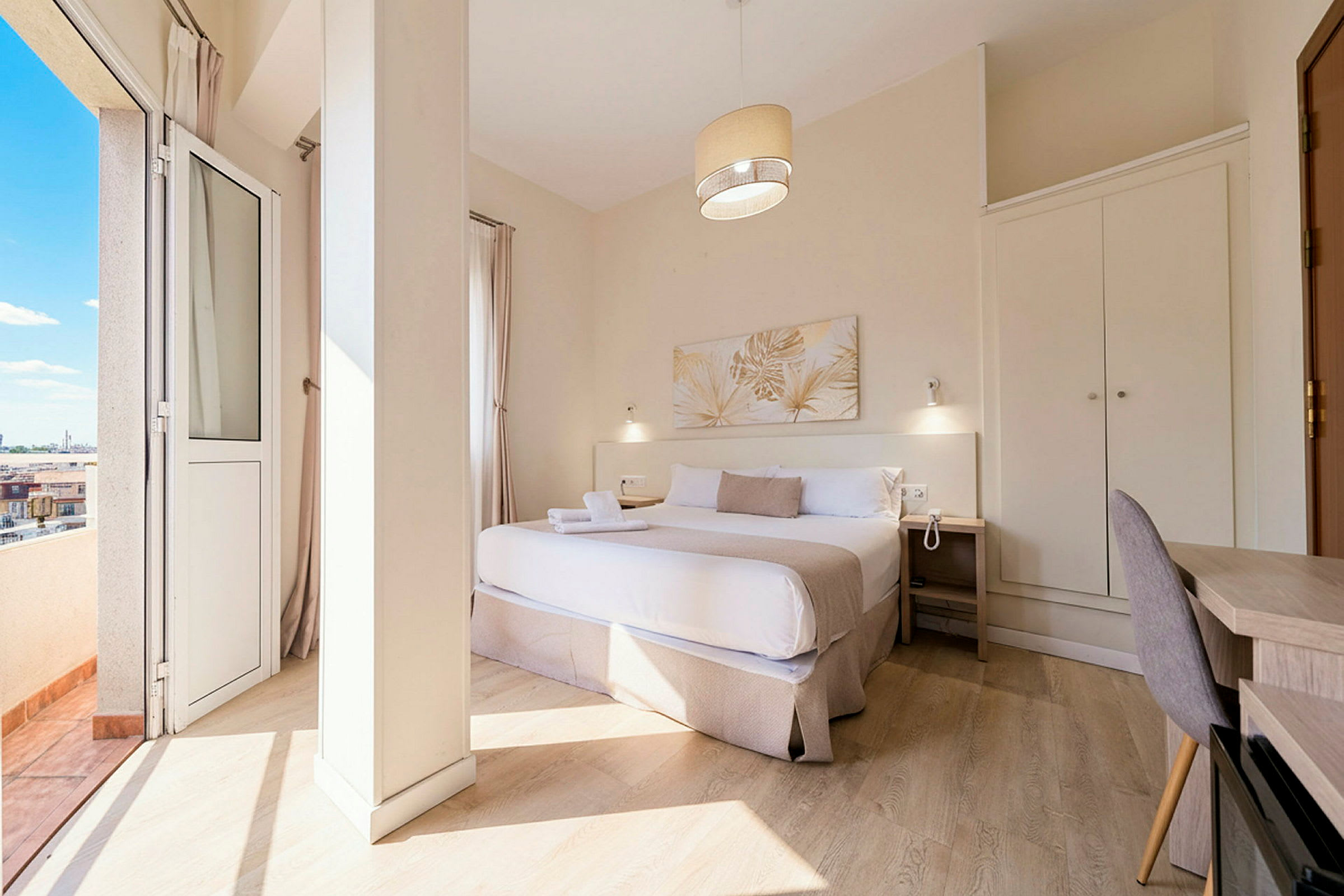 Et hotelværelse med en dobbeltseng, natbord, skrivebord og garderobe samt en balkon med udsigt. (AI-genereret tekst)