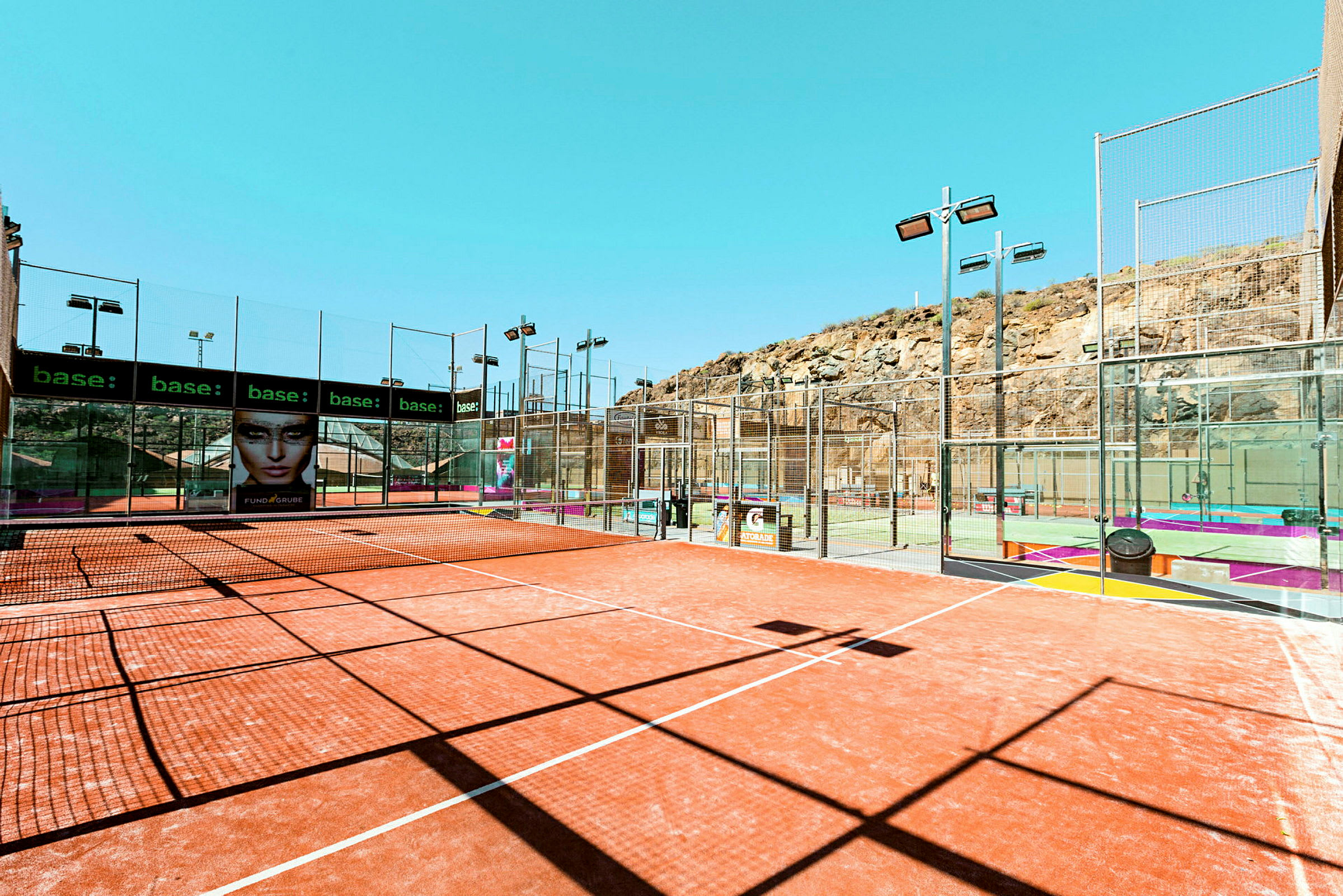 Udendørs padelbaner ved klippeterræn med net og omgivende hegn. (AI-genereret tekst)