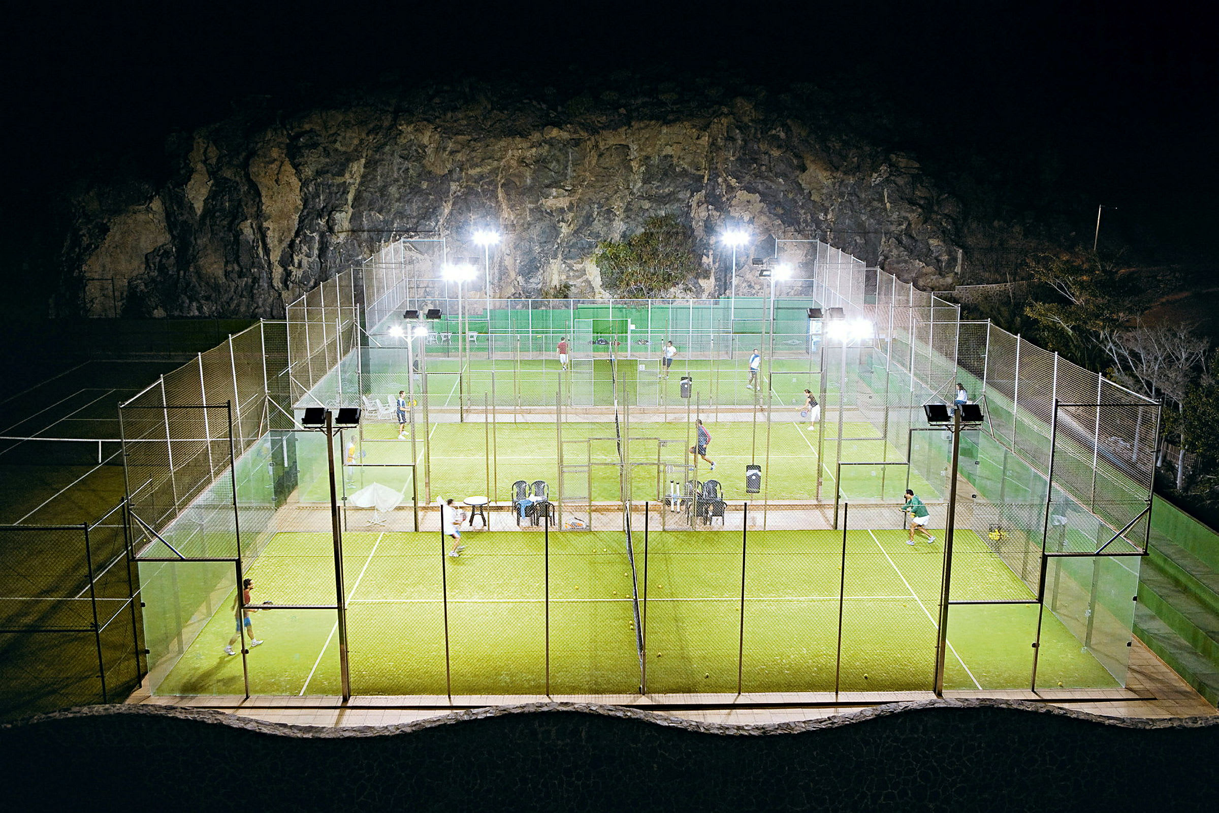 Udendørs padelbaner belyst om aftenen, spillere synlige på banen. (AI-genereret tekst)