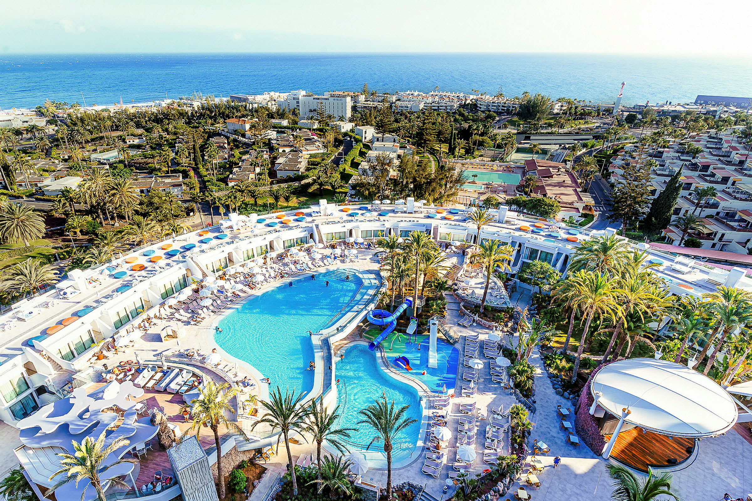 Luftfoto af et stort resort med poolområde og omgivet af palmer. (AI-genereret tekst)