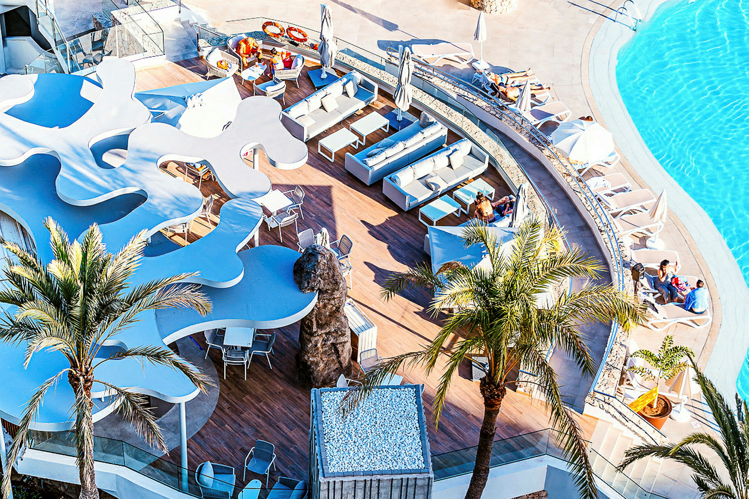 Udsigt over en pool og en terrasse med siddeområder og liggestole. (AI-genereret tekst)